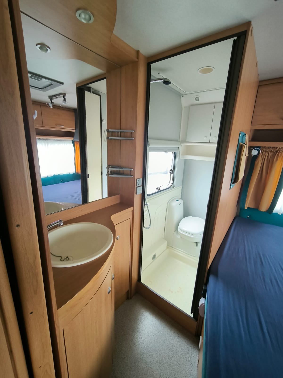 Interiér obytného auta s koupelnou, umyvadlem a lůžkem. Moderní a praktický design pro pohodlné cestování.