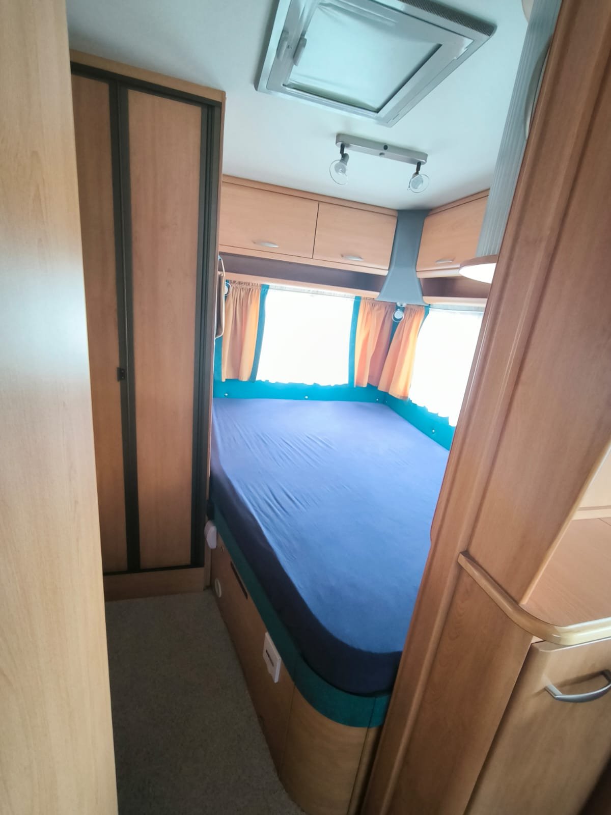 Obrázek interiéru karavanu s postelí a úložnými prostory. Skvělé pro pohodlné kempování a odpočinek.
