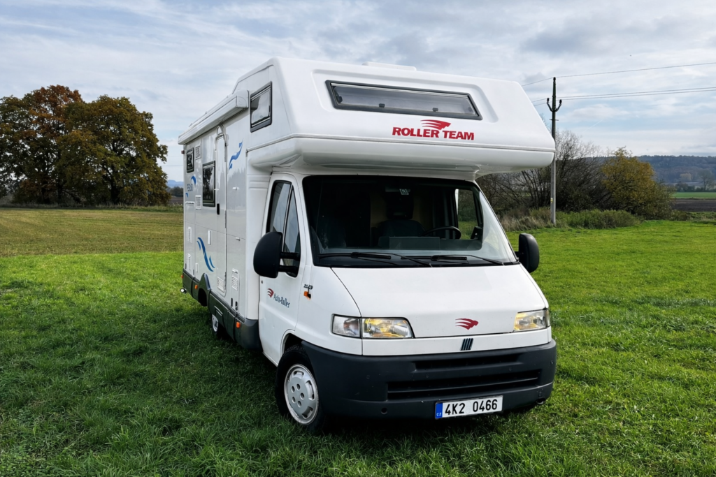 Obytné auto Roller Team parkované na travnaté ploše, ideální pro dobrodružství a kempování v přírodě.