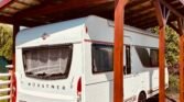 Karavan Bürstner pod přístřeškem, připravený na cesty s pohodlným zázemím.