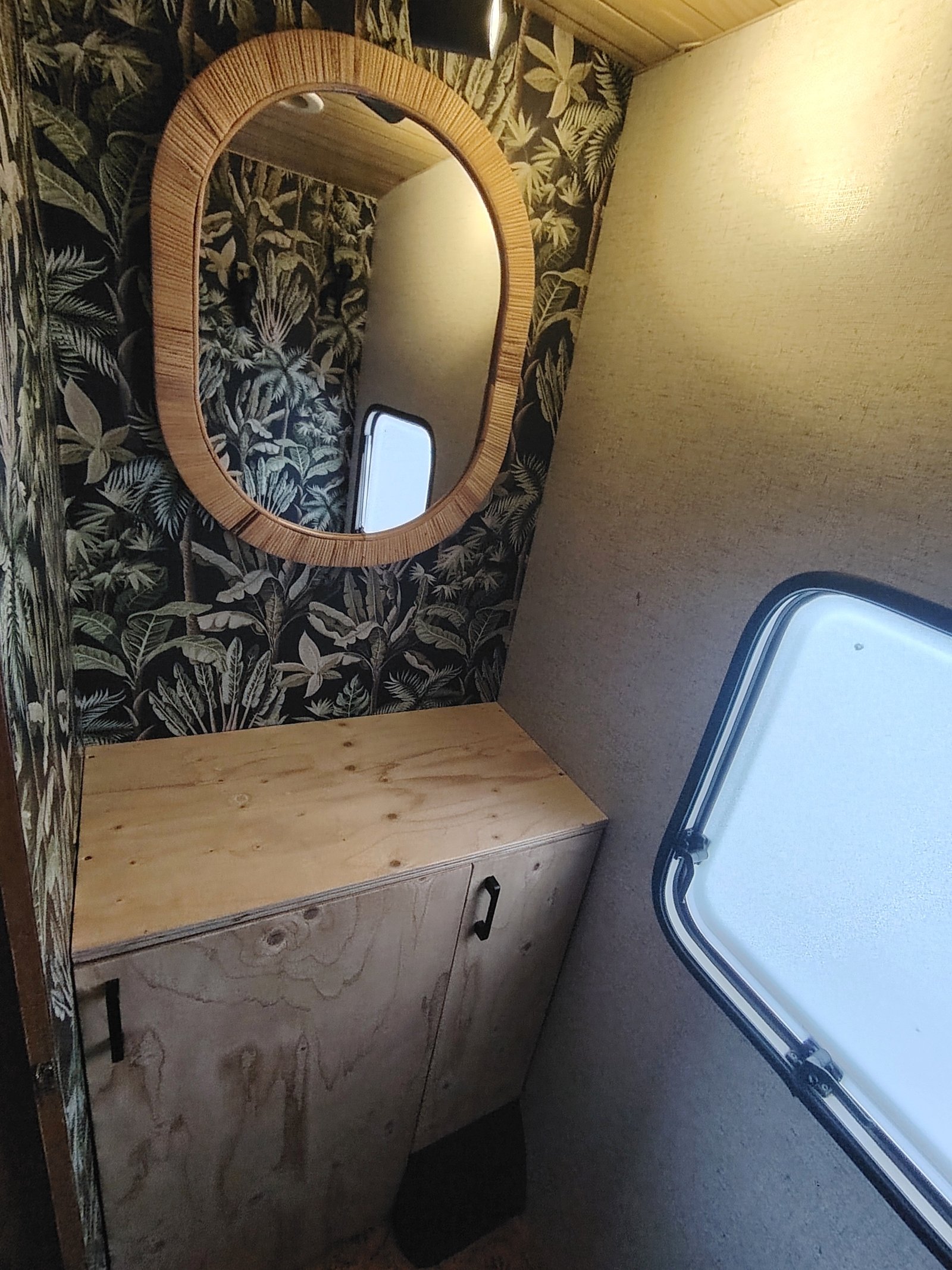 Interiér karavanu s přírodním dekorativním designem a odrazem zrcadla na stěně.