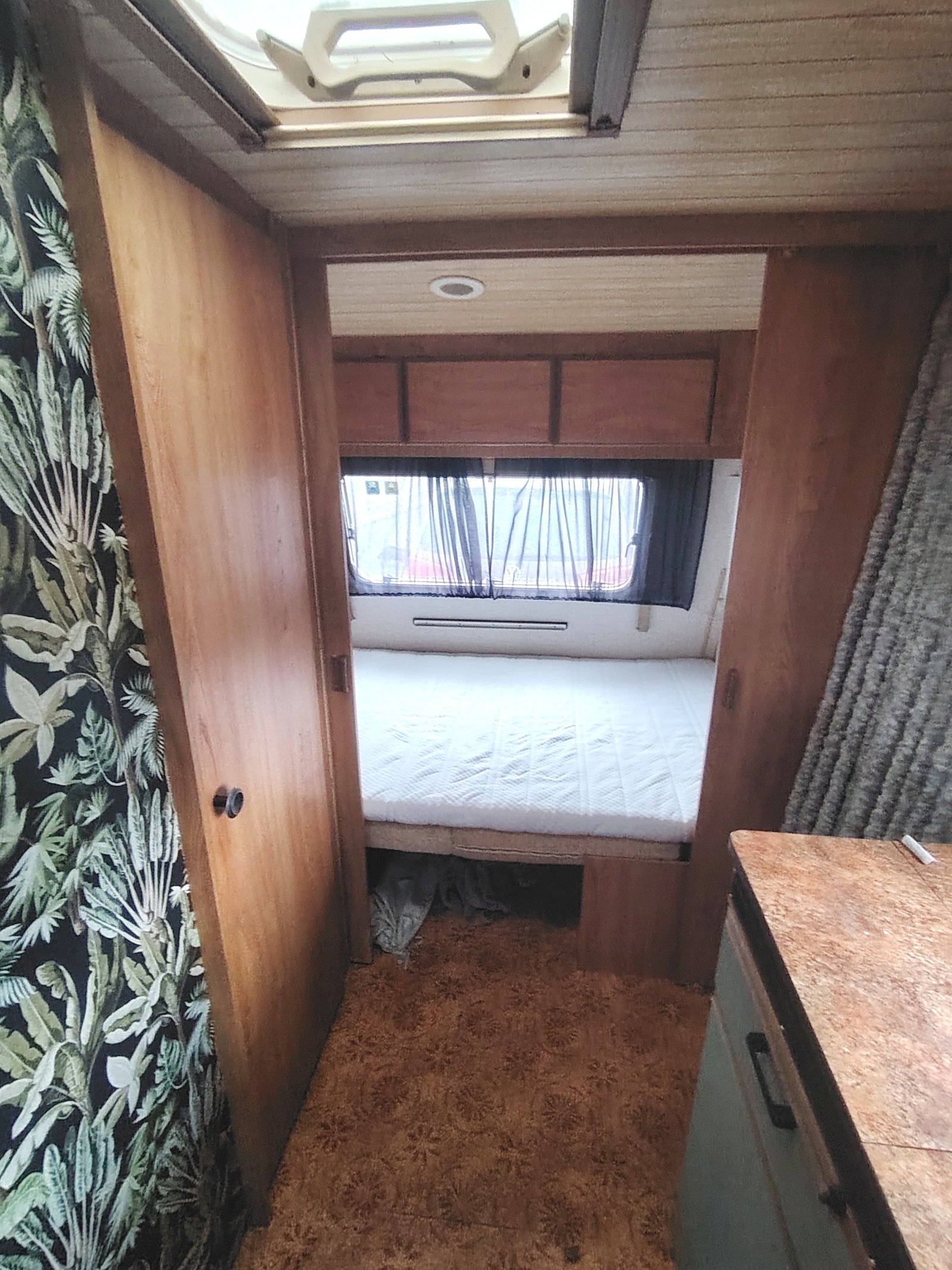 Interiér karavanu s postelí a kuchyňskou linkou, ideální pro pohodlné cestování a odpočinek.