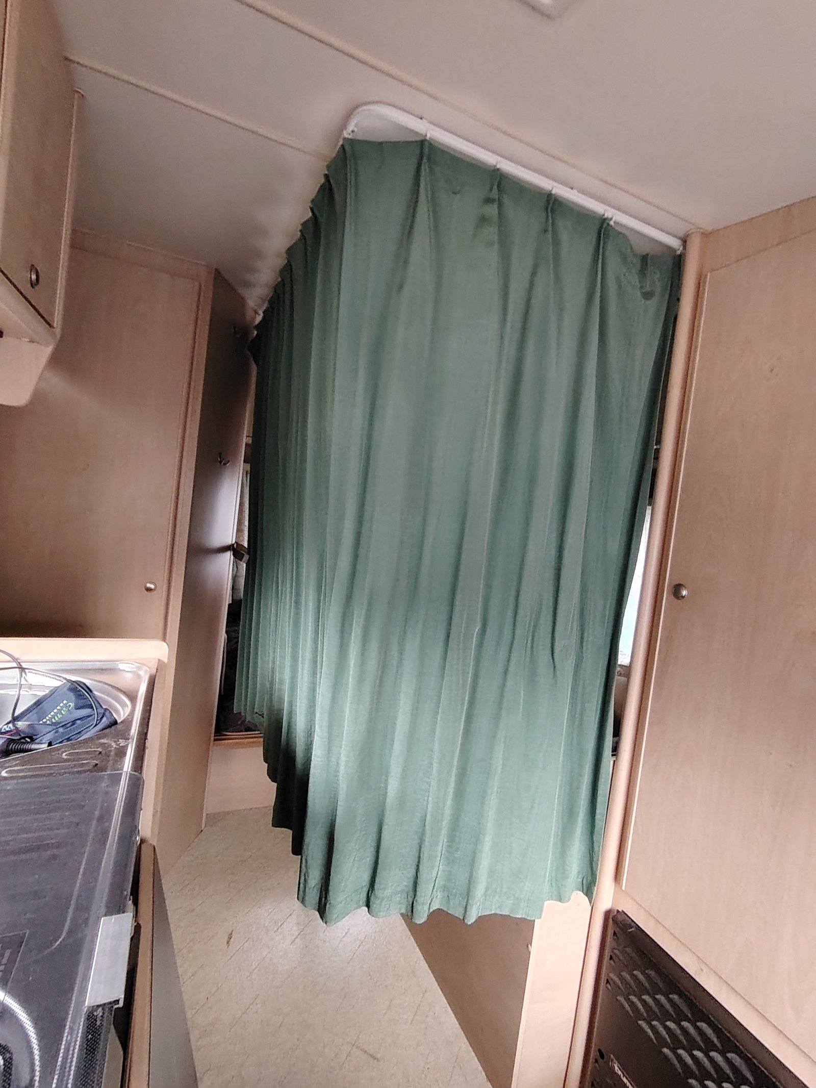 Obrázek interiéru obytného auta s kuchyňským koutem a závěsem. Značka a model nejsou viditelné.