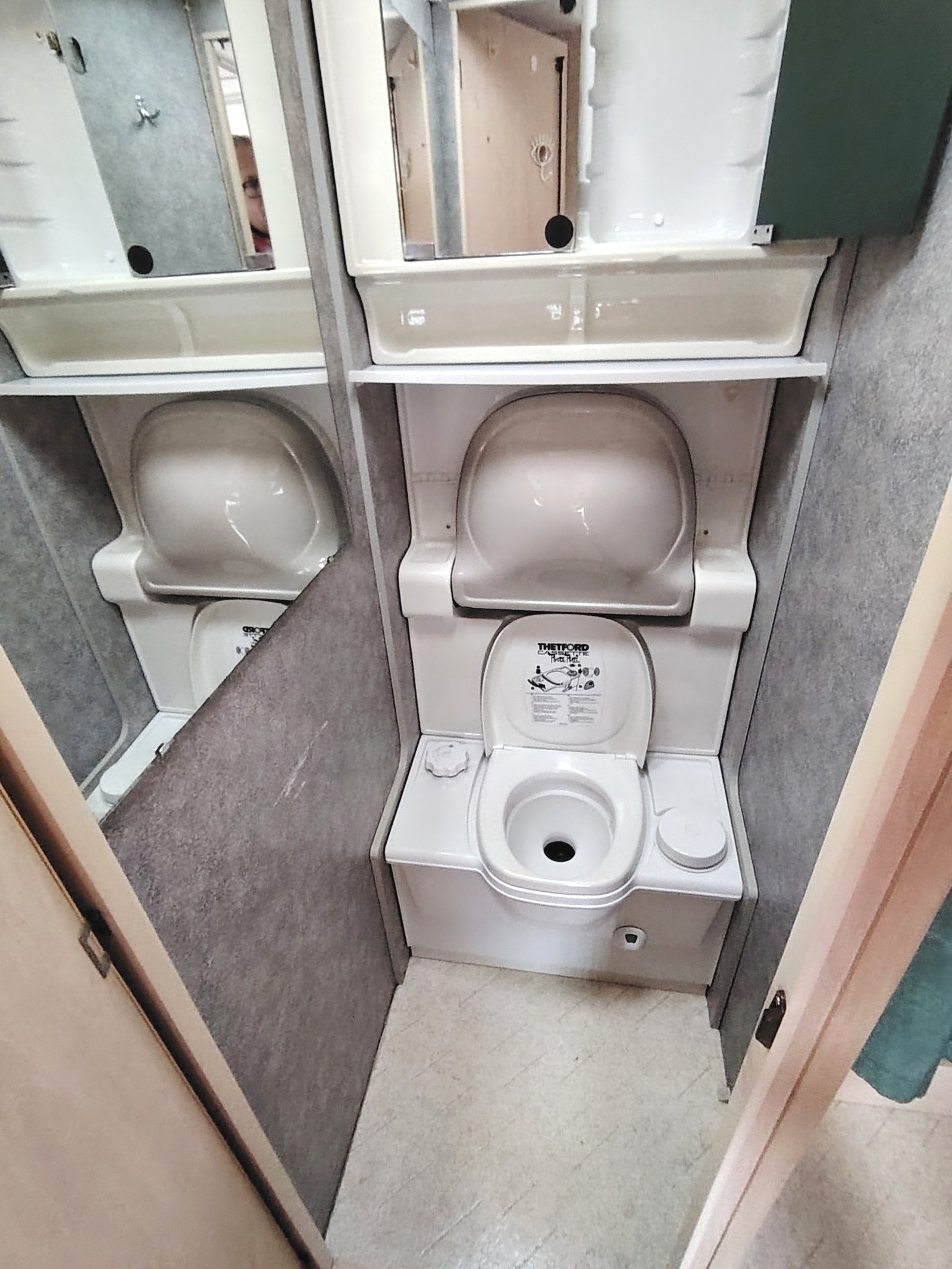 Koupelna v karavanu, jednoduchý toaletní systém s umyvadlem a zrcadlem. Elegantní design pro pohodlí na cestách.