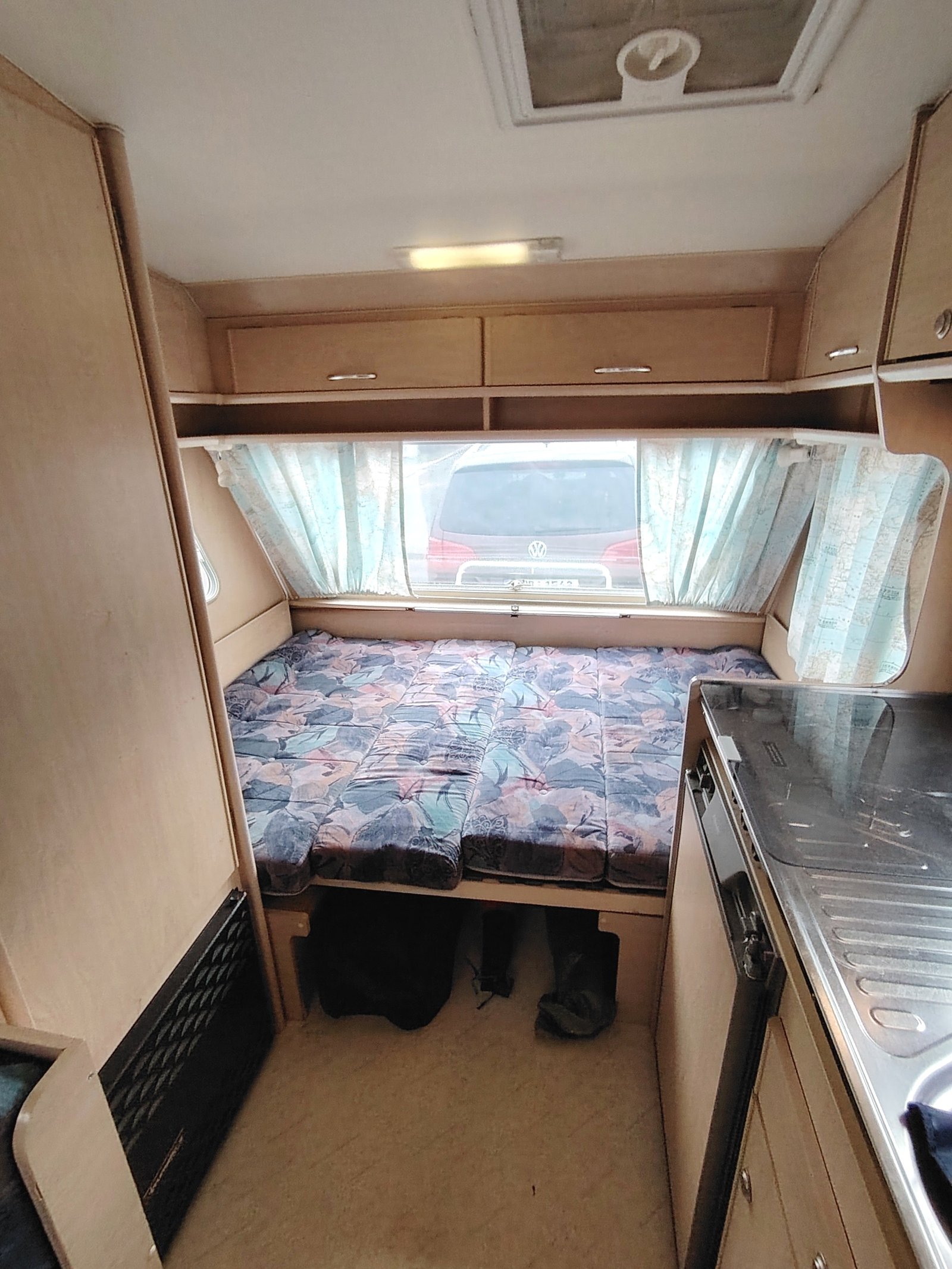 Interiér karavanu s rozkládacím lůžkem a kuchyňkou. Ideální pro pohodlné cestování a relaxaci.