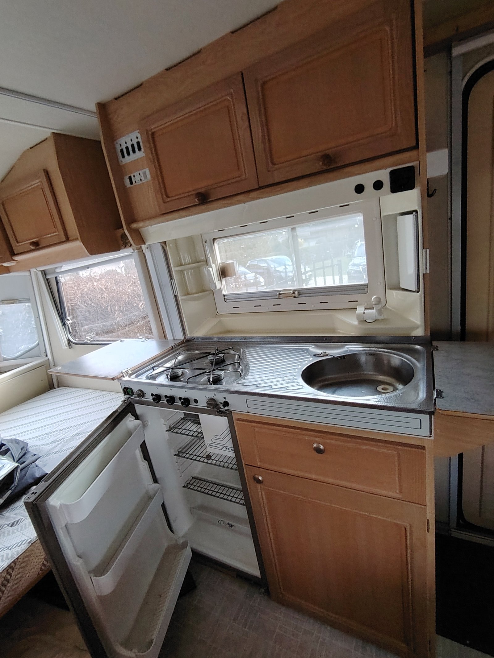 Obrázek interiéru karavanu s kuchyňským koutem, sporákem a lednicí pro pohodlné vaření na cestách.