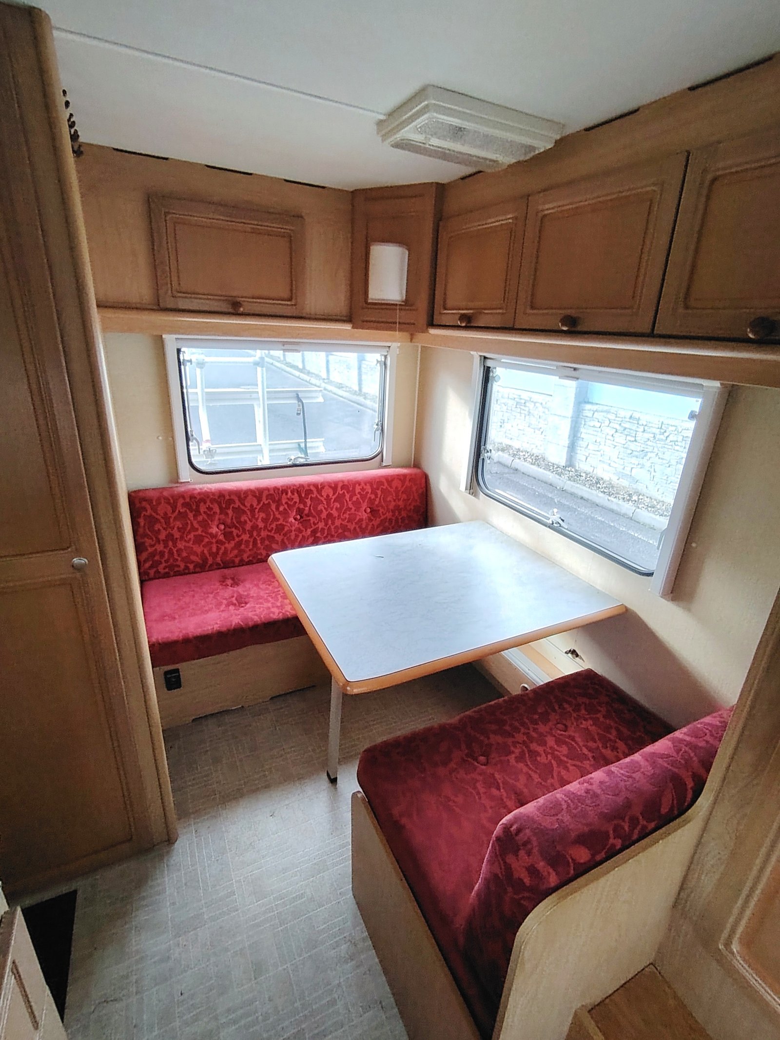 Obrázek interiéru karavanu s červenými sedacími částmi a stolem. Ideální pro pohodlné cestování a relaxaci.