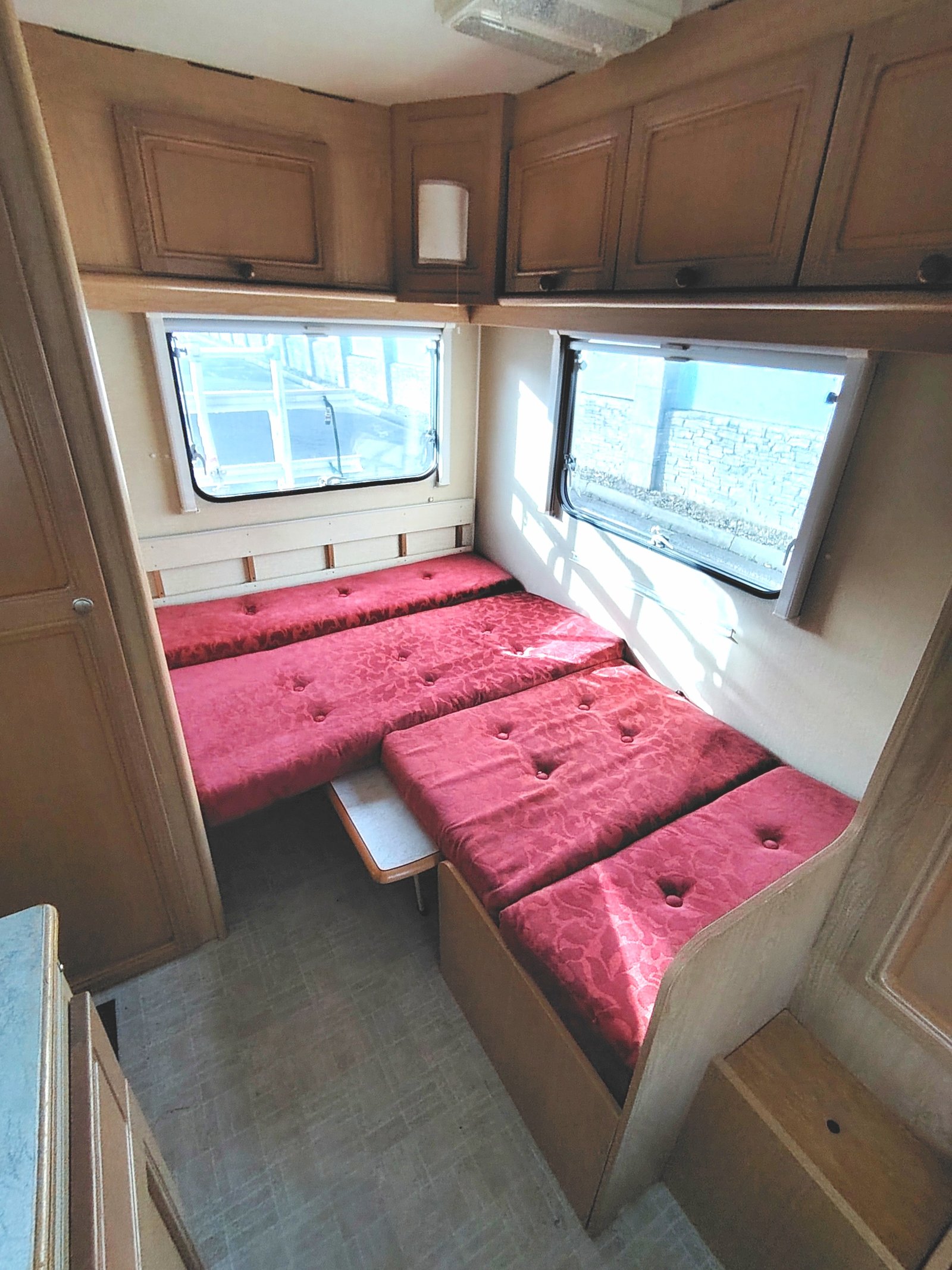 Interiér karavanu s červenými lůžky a osvětlením, ideální pro pohodlné cestování.