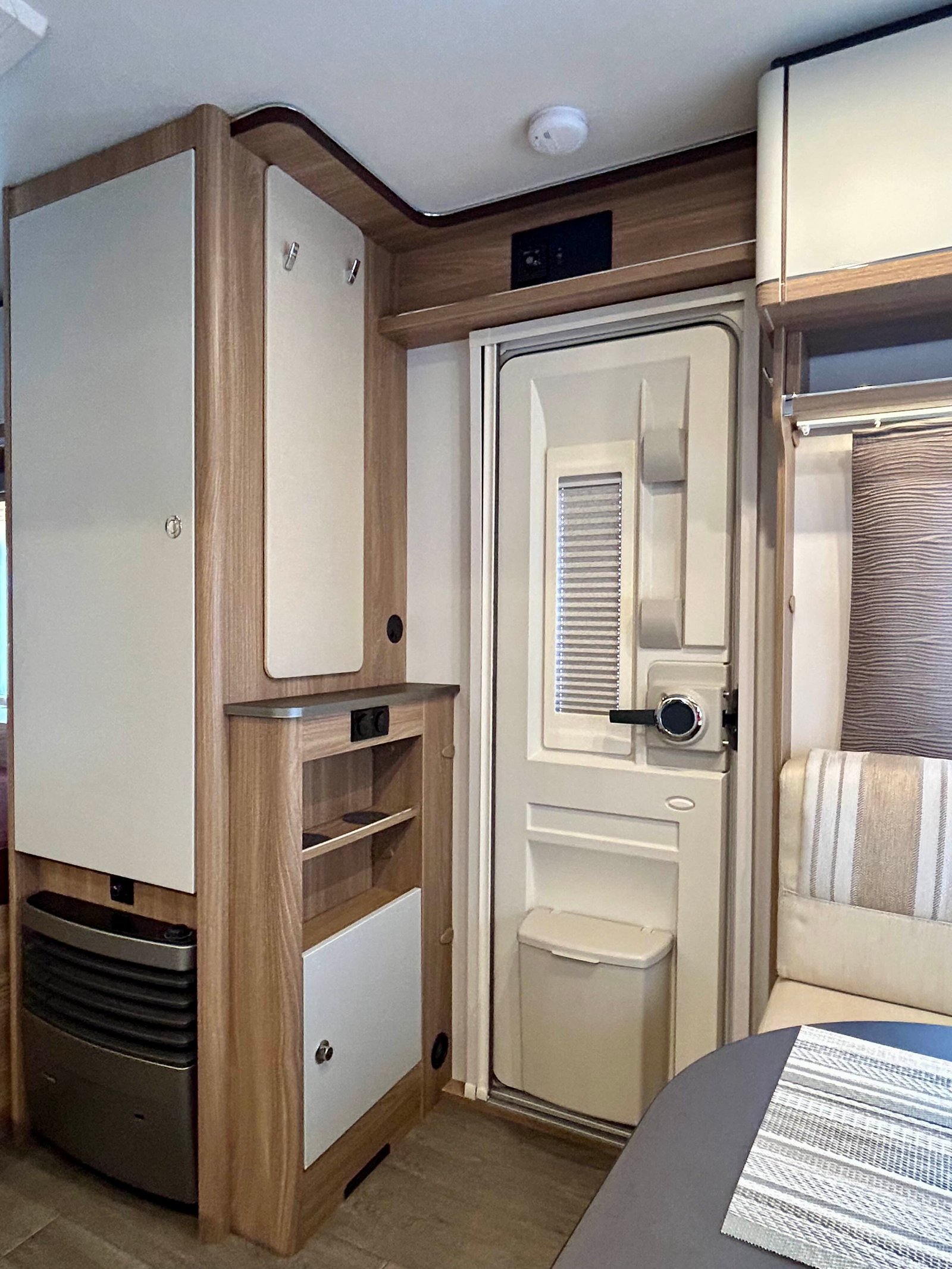 Obrázek zobrazuje interiér moderního karavanu s dřevěnými prvky a úložným prostorem.