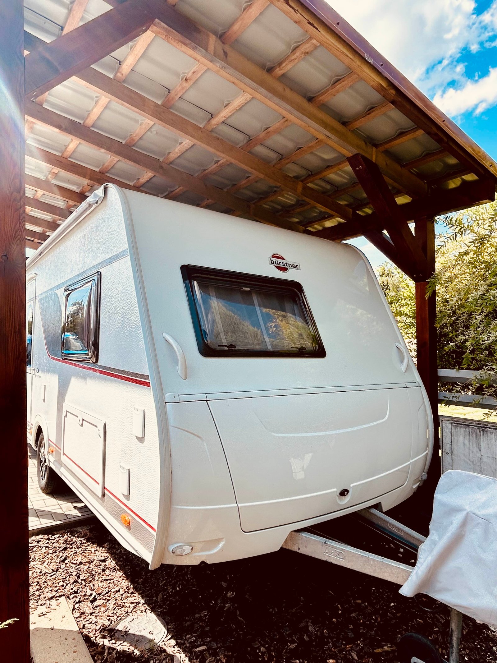 Karavan Bürstner pod přístřeškem, ideální pro letní dobrodružství a cestování.