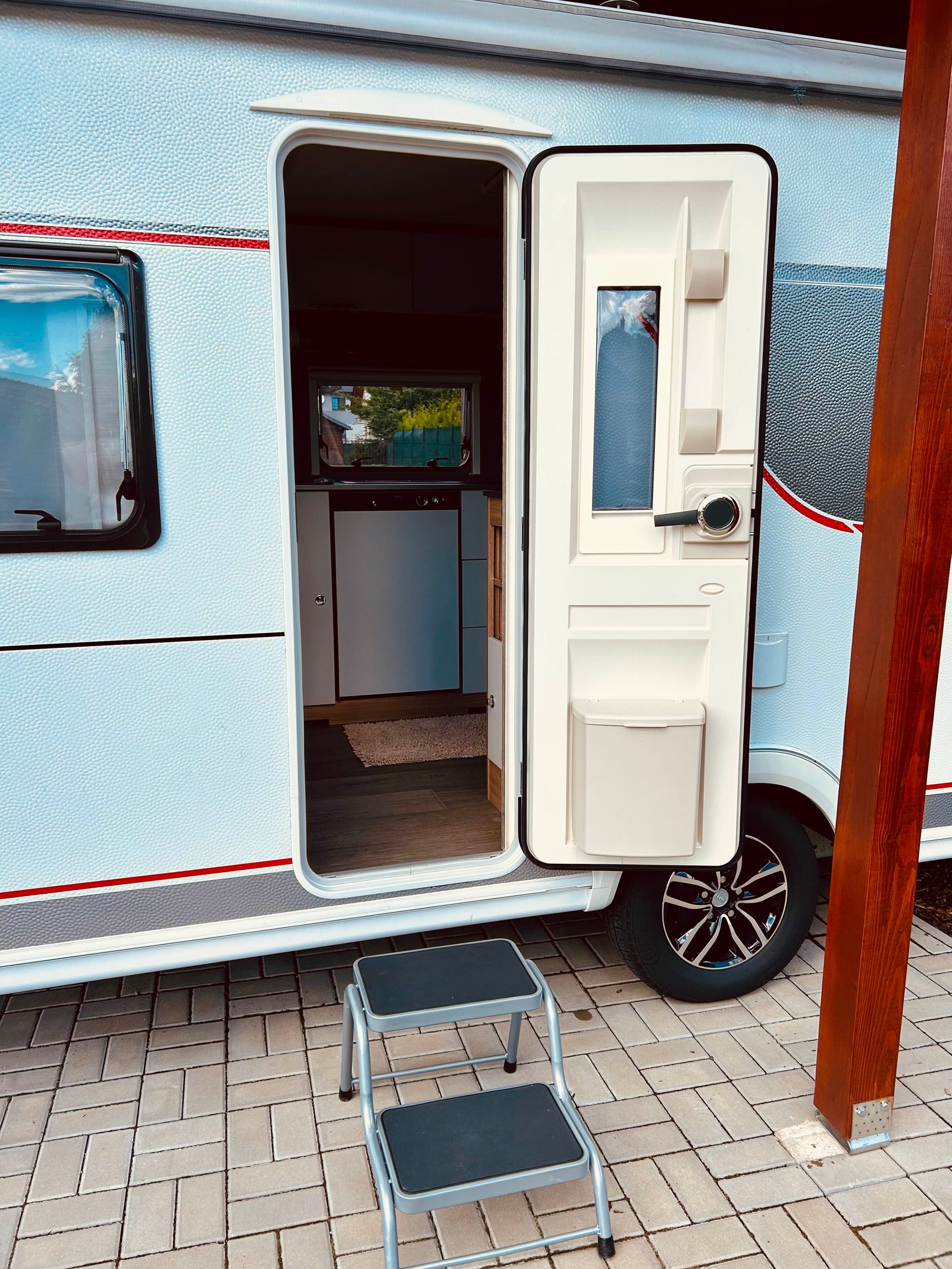 Obrázek zobrazuje karavan s otevřenými dveřmi a schůdky na vstup. Interiér je moderně vybaven.