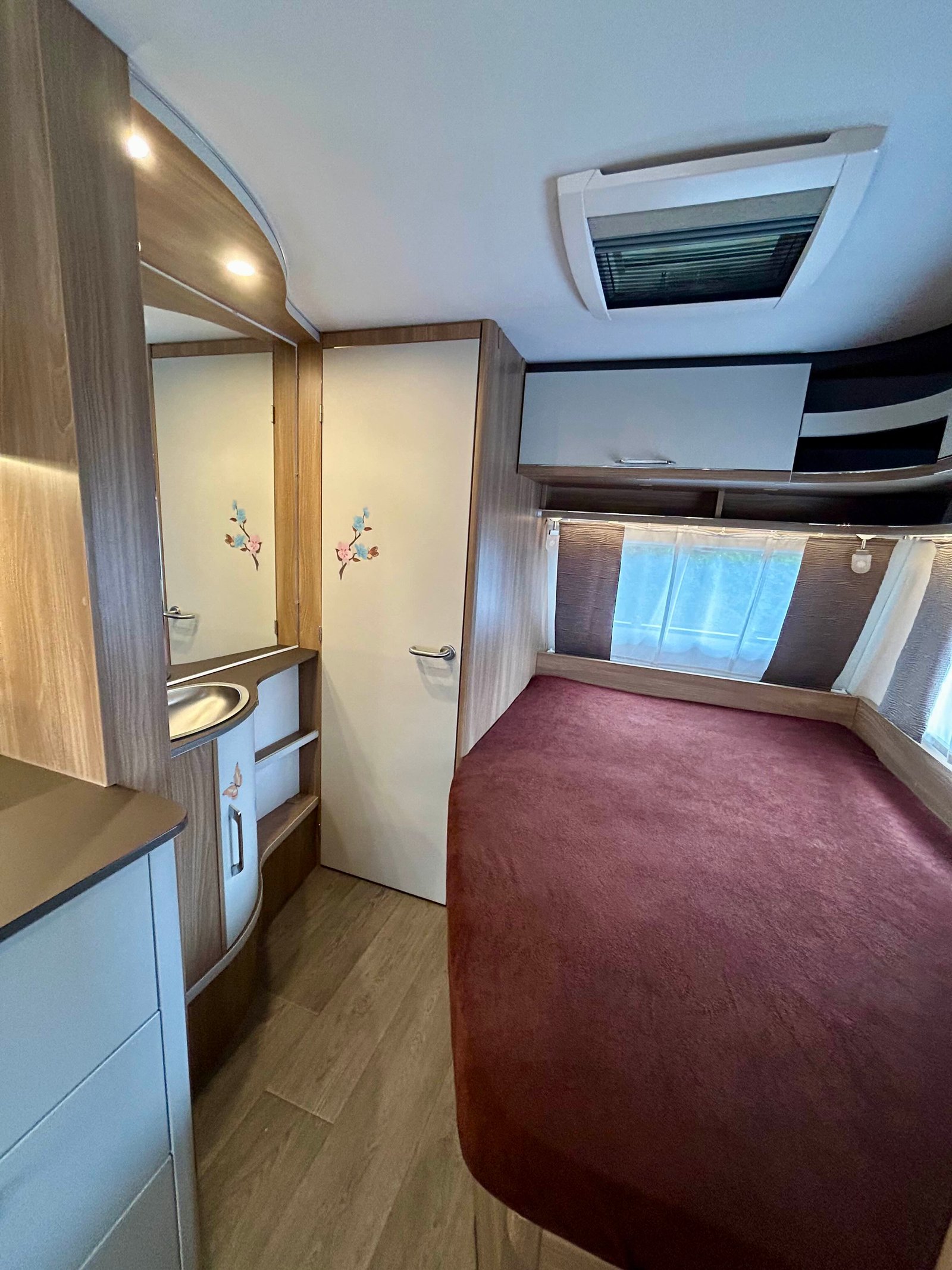 Interiér elegantního karavanu s dřevěnými prvky a komfortním lůžkem. Ideální pro pohodlné cestování.