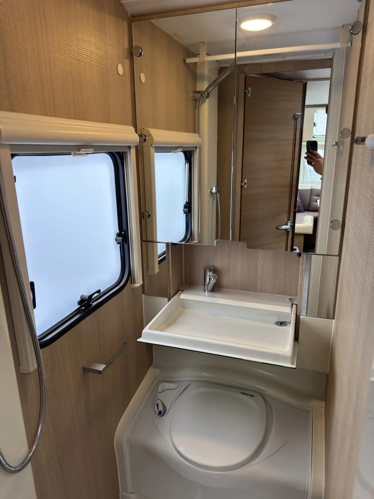 Obrázek interiéru karavanu s koupelnou a sprchovým koutem, moderní design a funkční prvky.