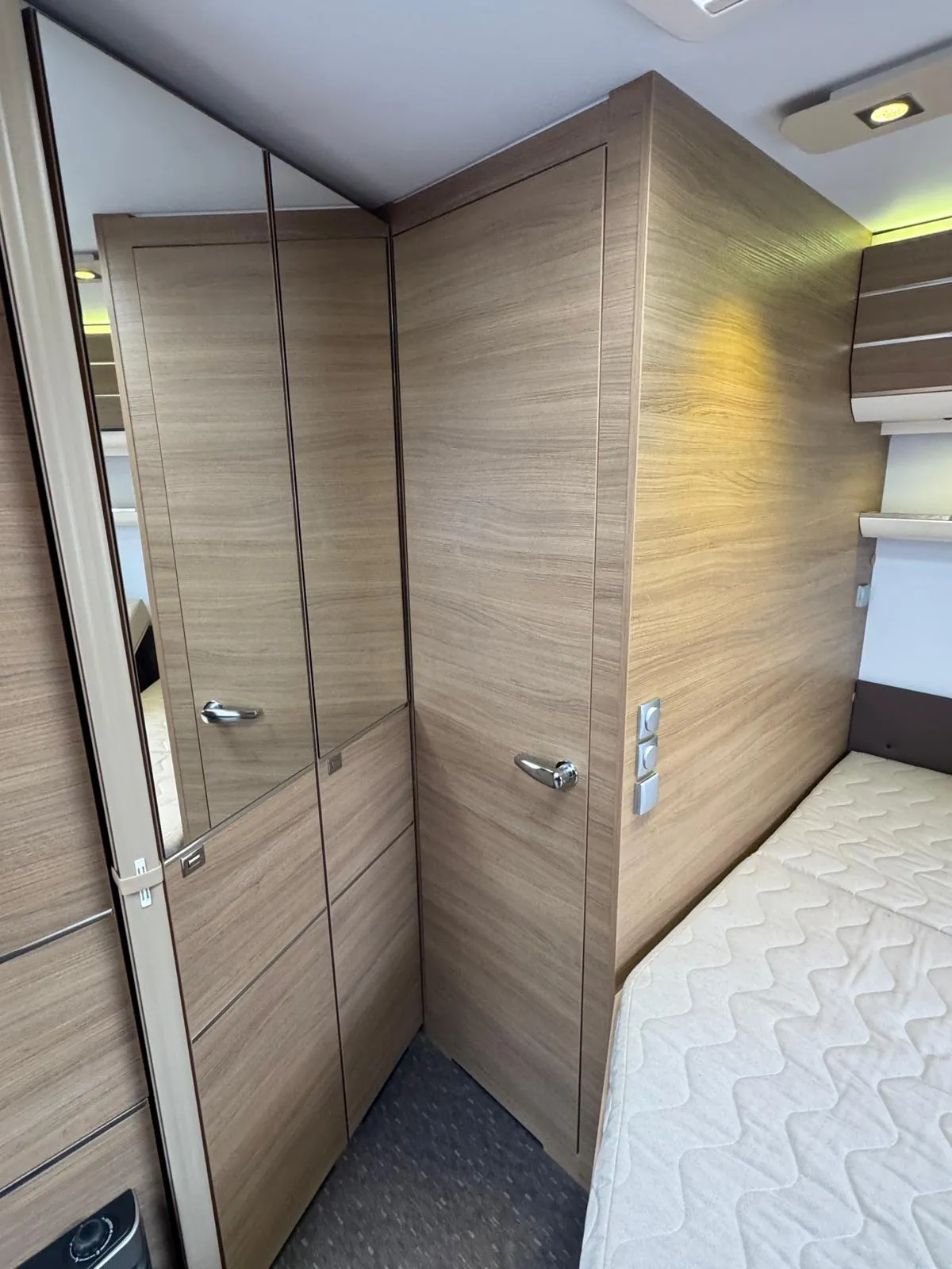 Obrázek interiéru obytného vozu, zaměřený na skříně a prostor na spaní, moderní design s dřevěnými prvky.