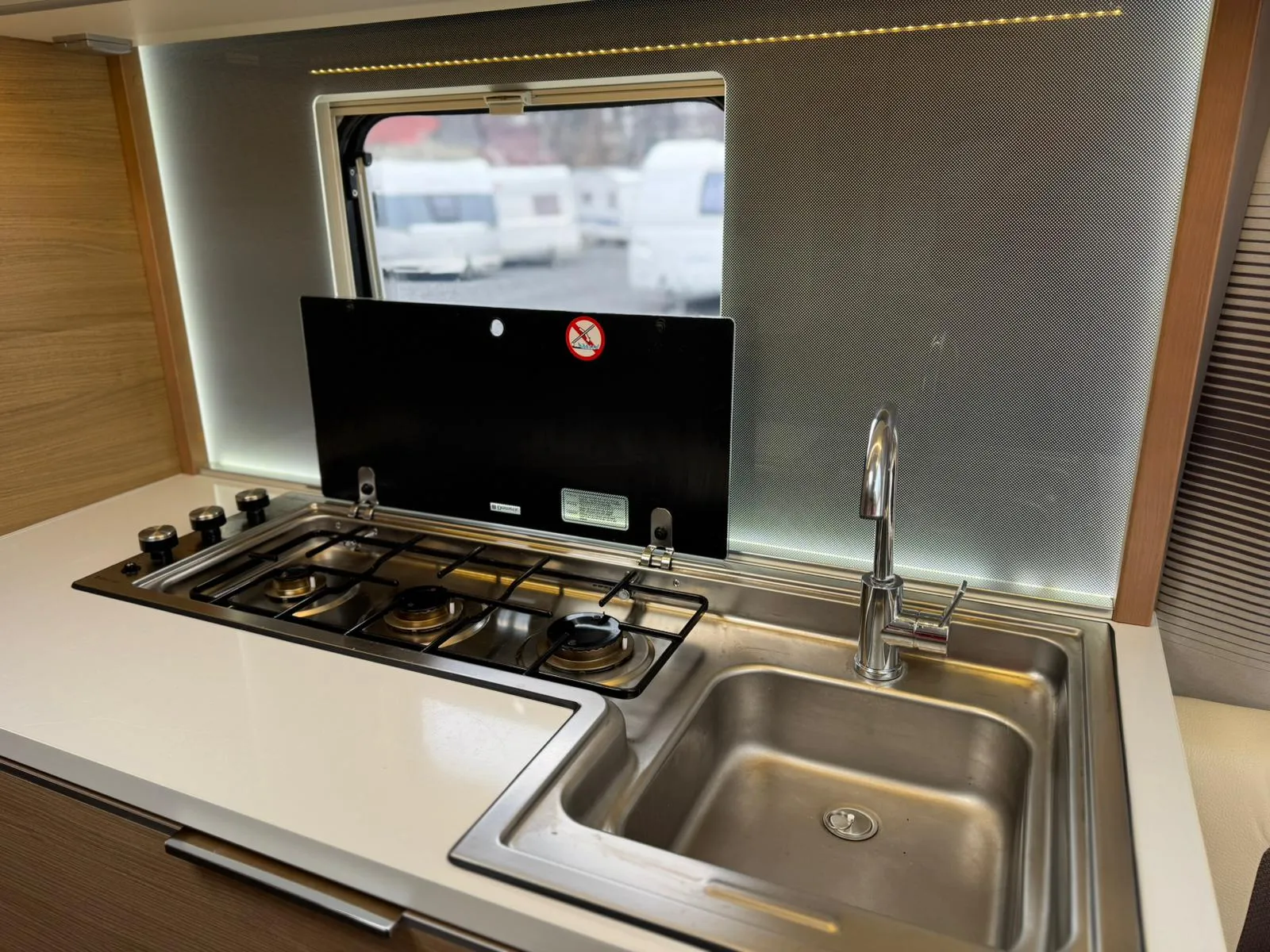 Kuchyňka s kovovým dřezem a sporákem je součástí karavanu. Moderní design pro pohodlné vaření na cestách.