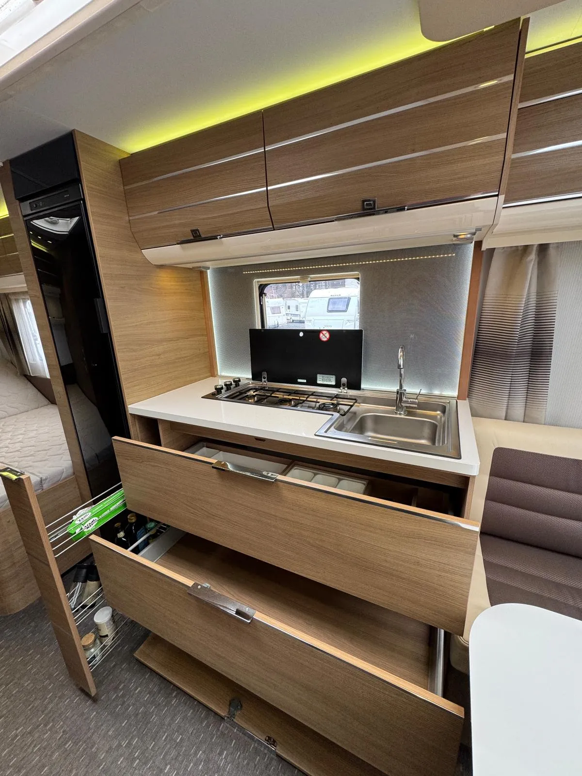 Interiér obytného vozu s moderními skříněmi, sporákem a dřezem. Komfortní a praktický prostor pro dobrodružství.