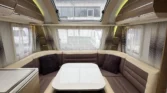 Obrázek interiéru karavanu s útulným sezením, stolem a velkým střešním oknem. Ideální pro pohodové cestování.