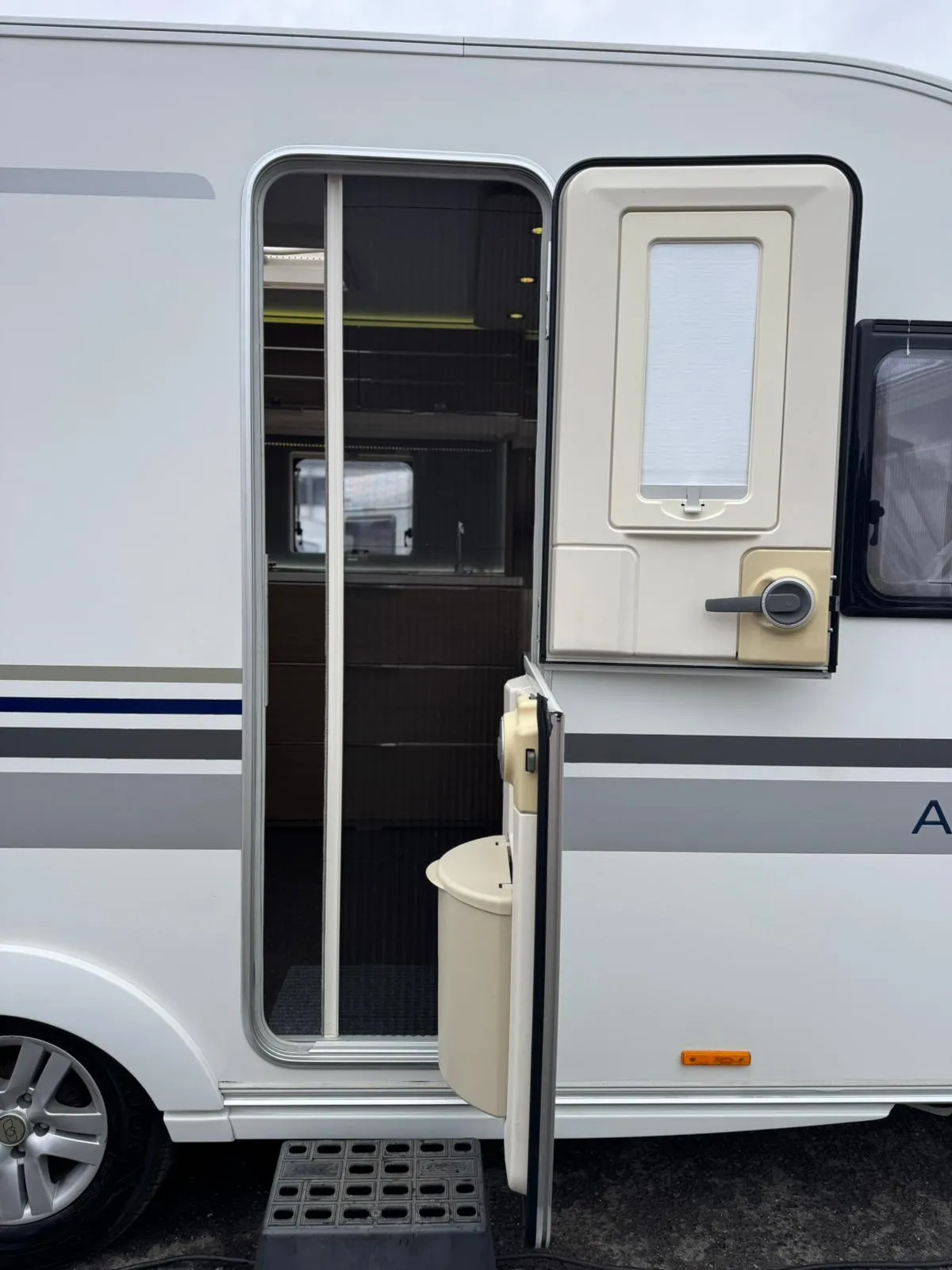 Obrázek zachycuje elegantní karavan s otevřenými dveřmi, připravený na dobrodružství.