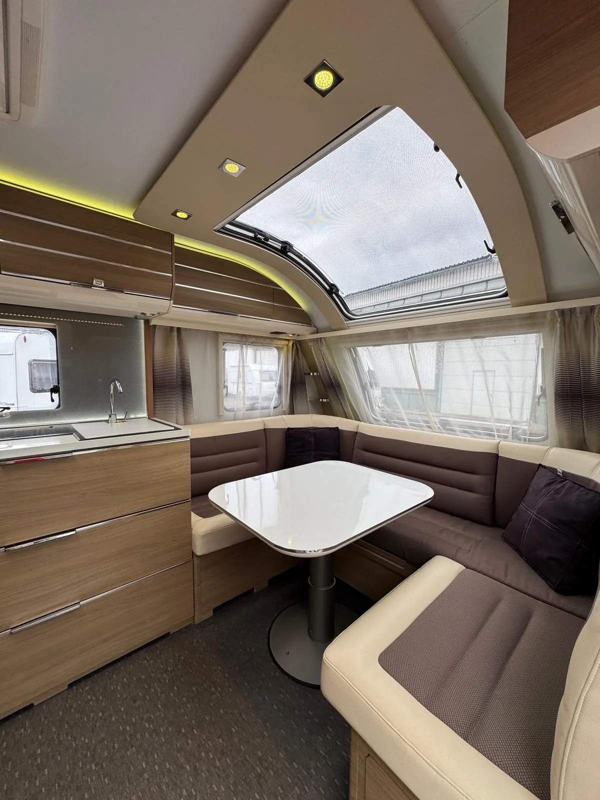 Interiér karavanu s příjemným posezením a kuchyňským koutem. Moderní design a dostatek světla.