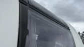 Obrázek zobrazuje detail okna na karavanu, ideální pro pohodlné cestování.