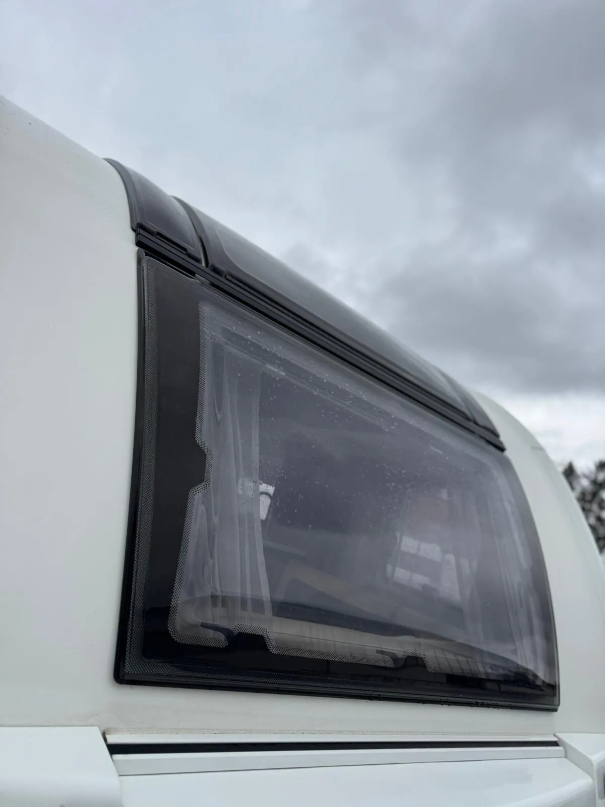 Obrázek zobrazuje detail okna na karavanu, ideální pro pohodlné cestování.