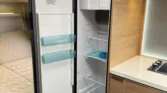 Obrázek znázorňuje kuchyňský kout s chladničkou v obytném autě. Moderní design interiéru pro pohodlné cestování.
