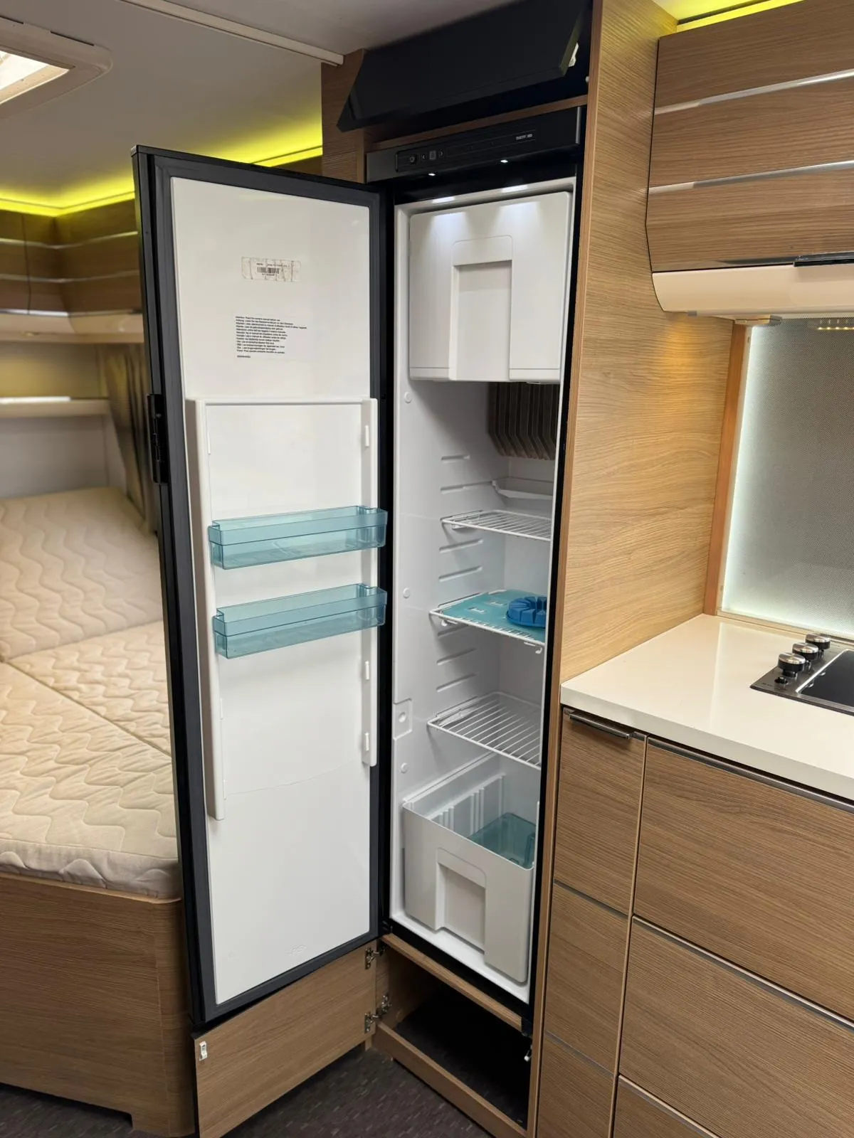 Obrázek znázorňuje kuchyňský kout s chladničkou v obytném autě. Moderní design interiéru pro pohodlné cestování.