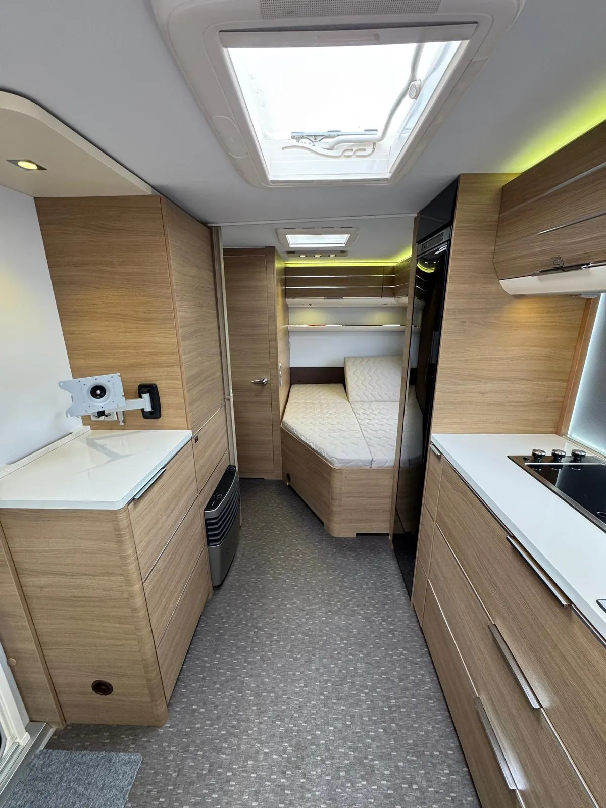 Obrázek interiéru karavanu s dřevěným designem a moderním vybavením. Žádné viditelné logo nebo model.