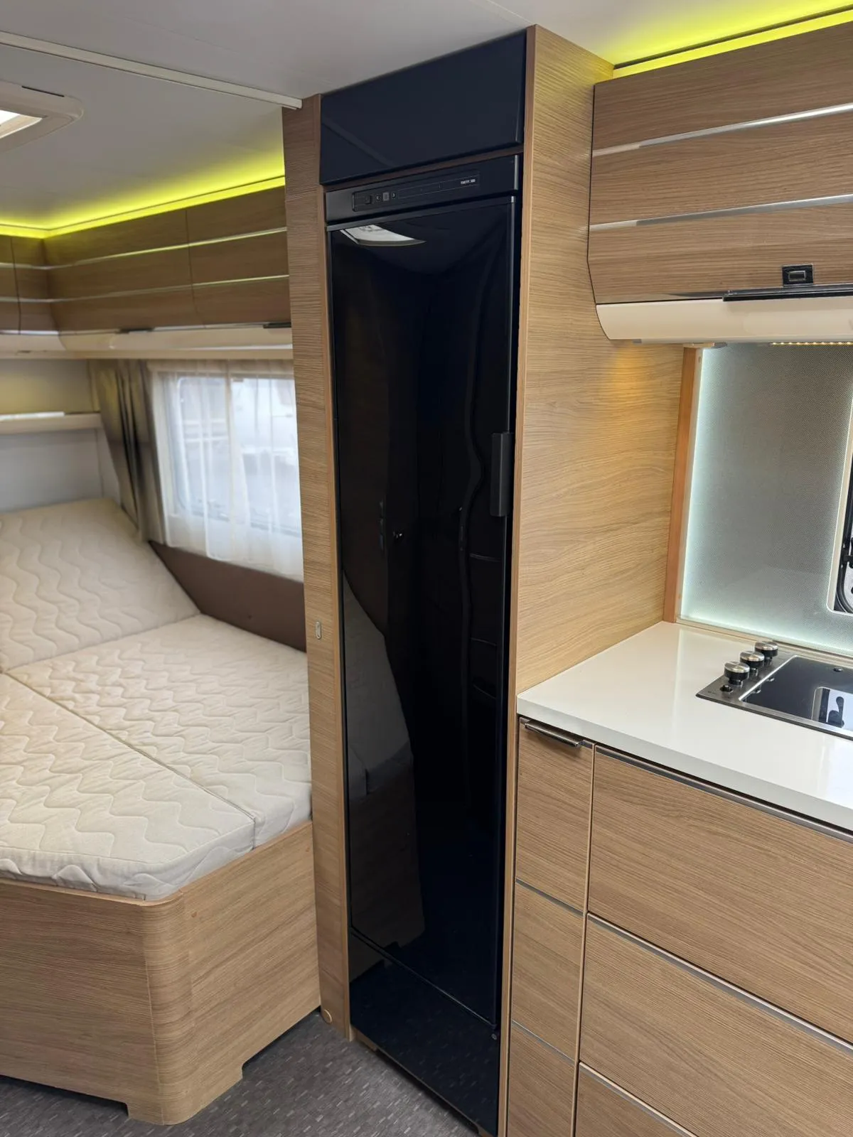 Obrázek interiéru moderního karavanu, který nabízí pohodlné spaní a vybavení pro vaření.