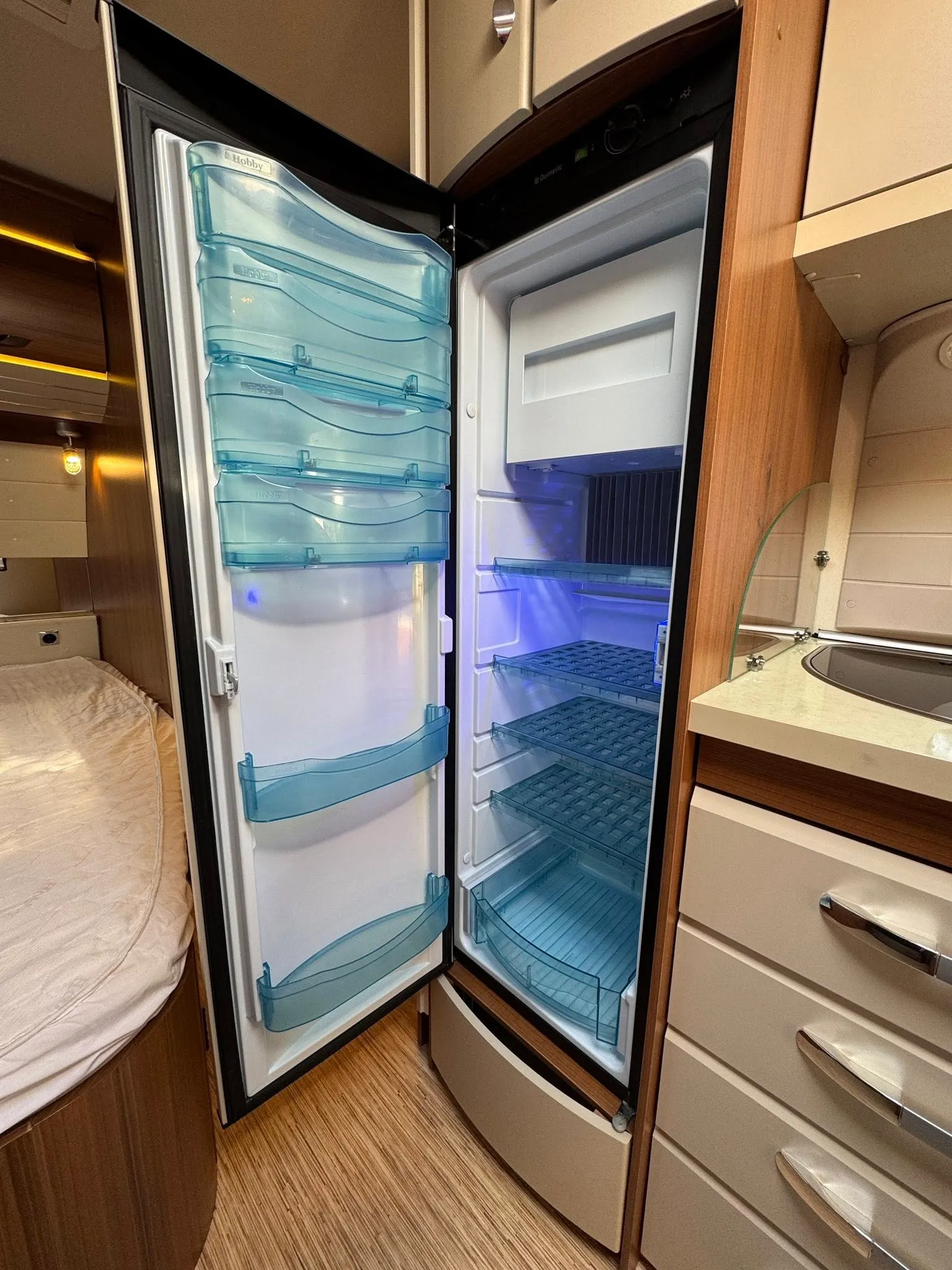 Obrázek představuje lednici v karavanu Hobby, ideální pro uchování potravin během cestování.