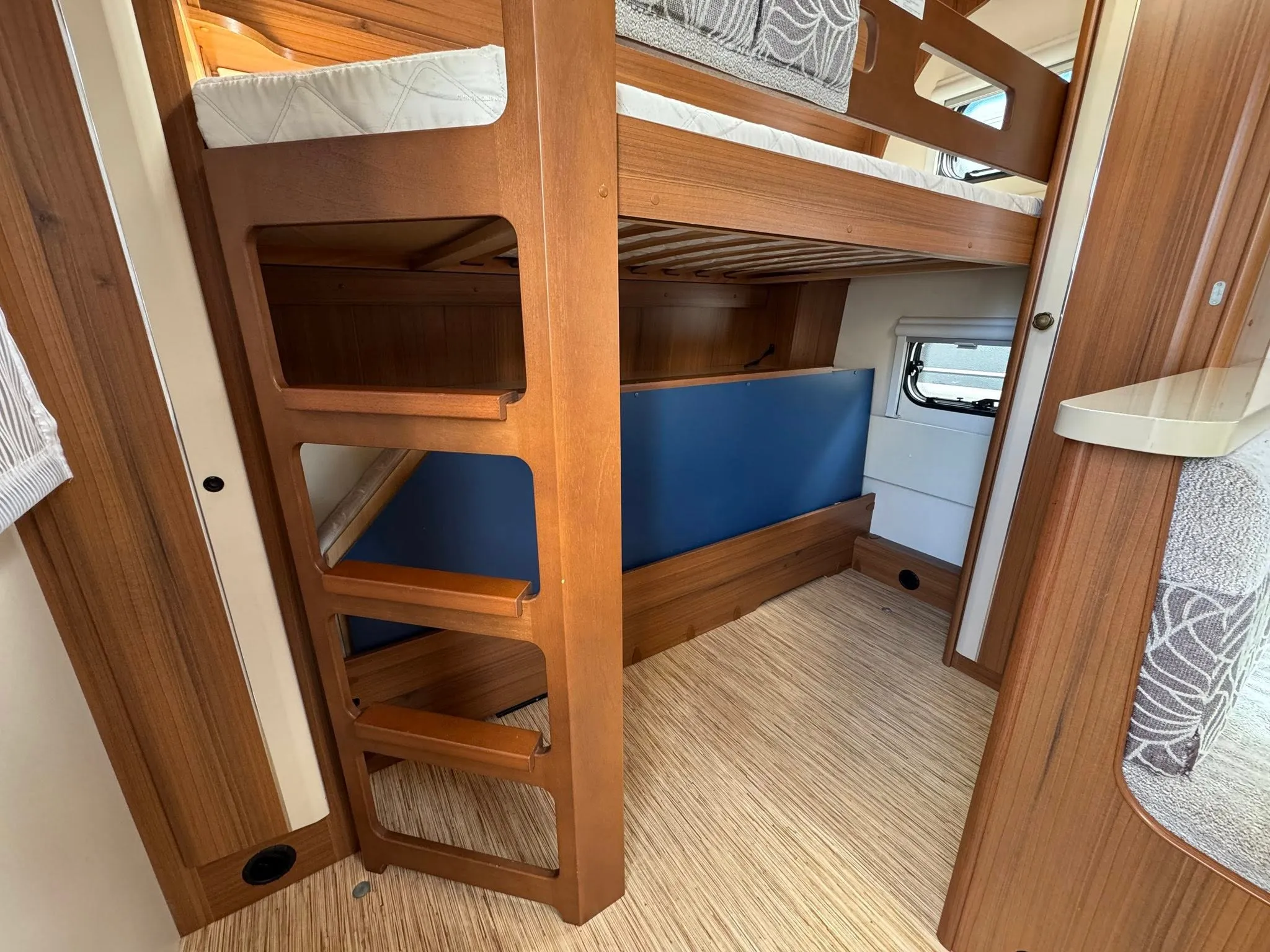 Detail interiéru karavanu s patrovou postelí a dřevěnými prvky. Ideální pro pohodlné cestování.