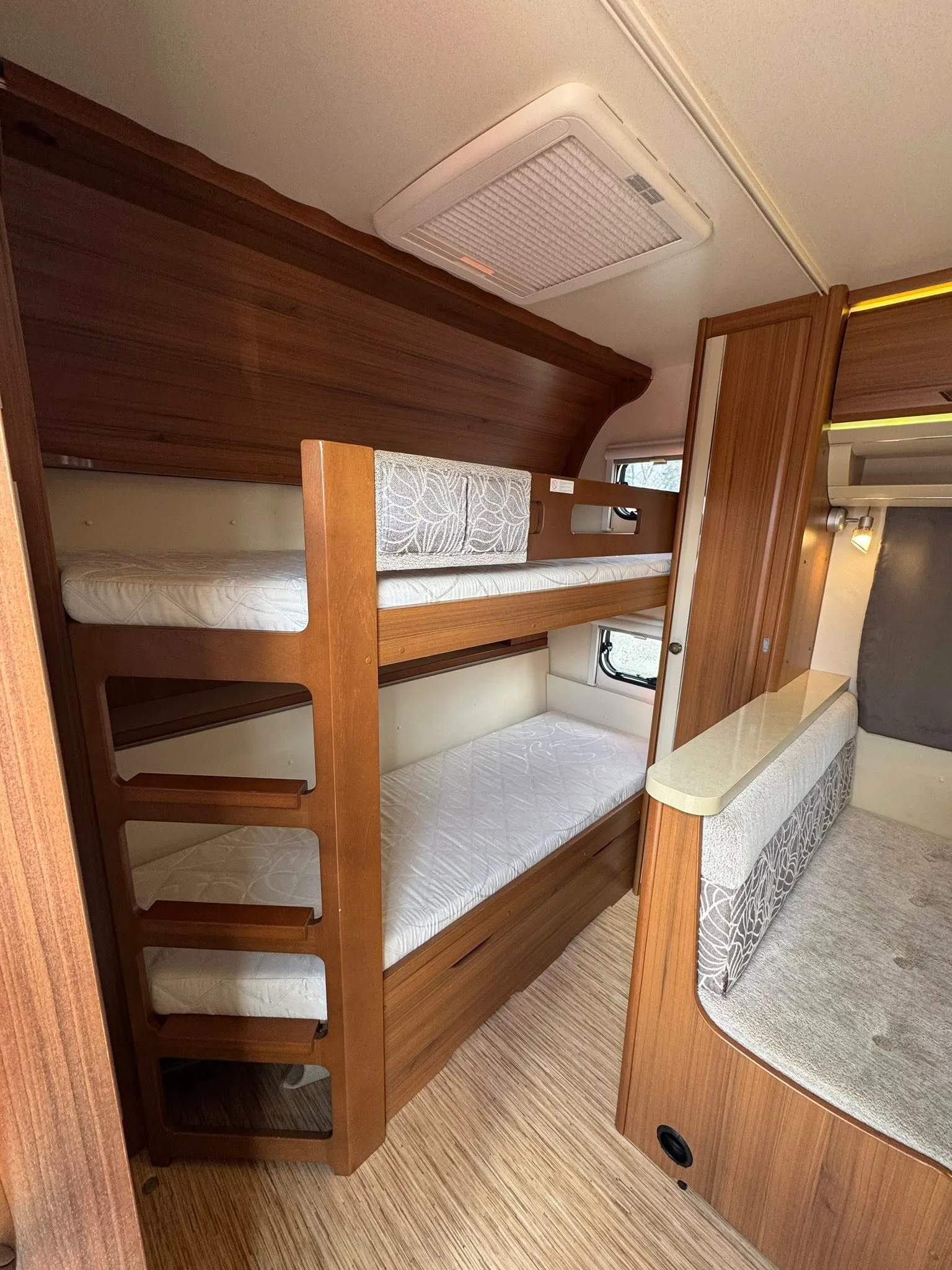 Moderní interiér obytného auta s patrovými postelemi a dřevěnými dekoracemi. Ideální pro pohodlné cestování.