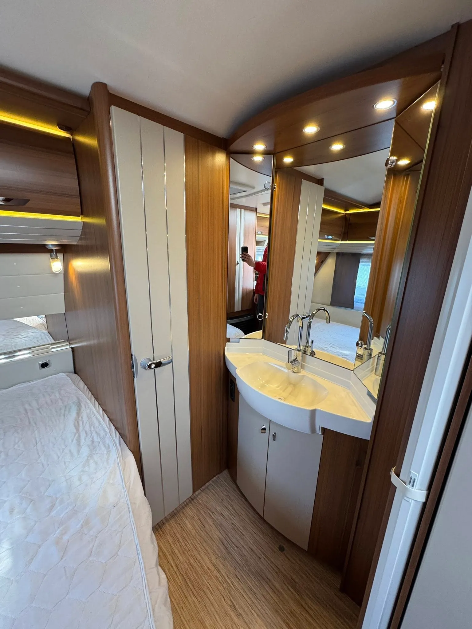 Obrázek interiéru karavanu s moderním designem, pohodlným lůžkem a koupelnovým koutem.