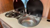 Kuchyňský kout obytného auta se dvoma vařiči a umyvadlem. Moderní design, ideální pro kempaření.