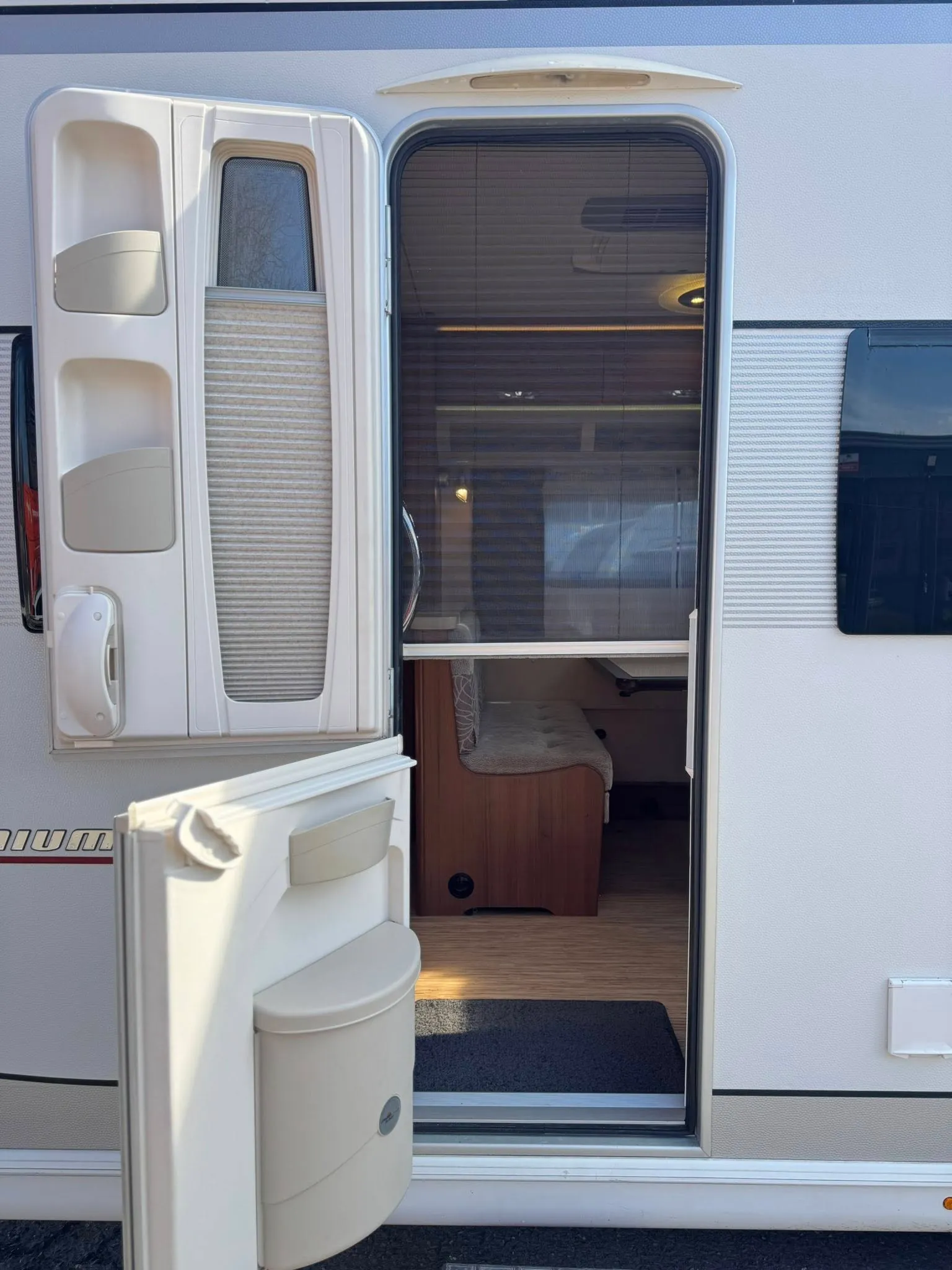 Obrázek interiéru karavanu, otevřené dveře s pohodlným posezením a moderním vybavením.