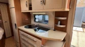Interiér karavanu s moderními kuchyňskými prvky a úložným prostorem. Vhodný pro pohodlné cestování.