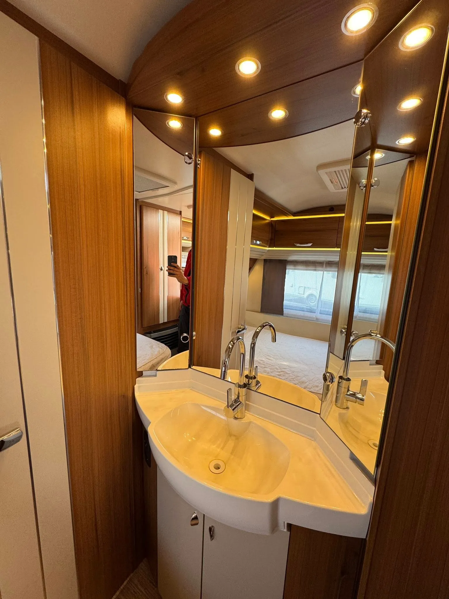 Obrázek interiéru karavanu s moderním umyvadlem a zrcadly. Příjemné osvětlení a dřevěné prvky dotvářejí atmosféru.