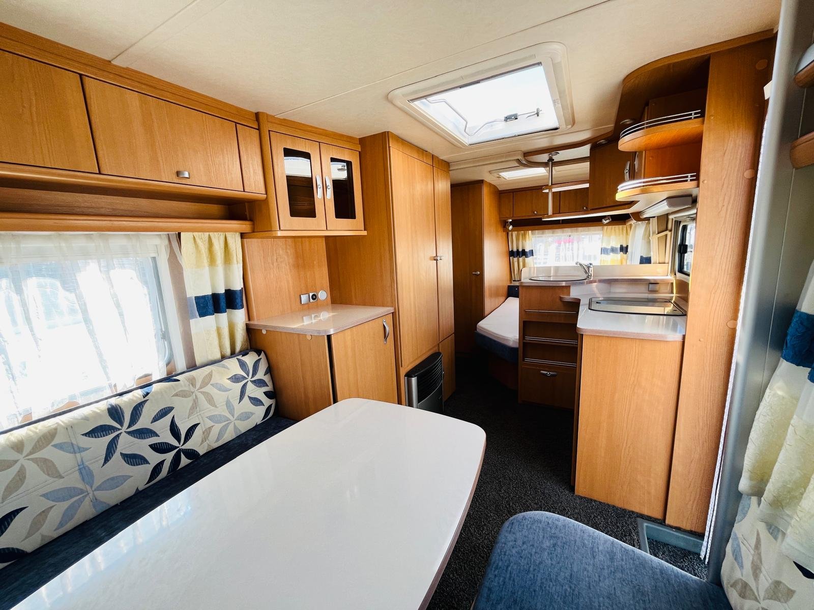 Interiér karavanu s dřevěným nábytkem a kuchyňským koutem. Prostorný a útulný design pro komfortní pobyt.