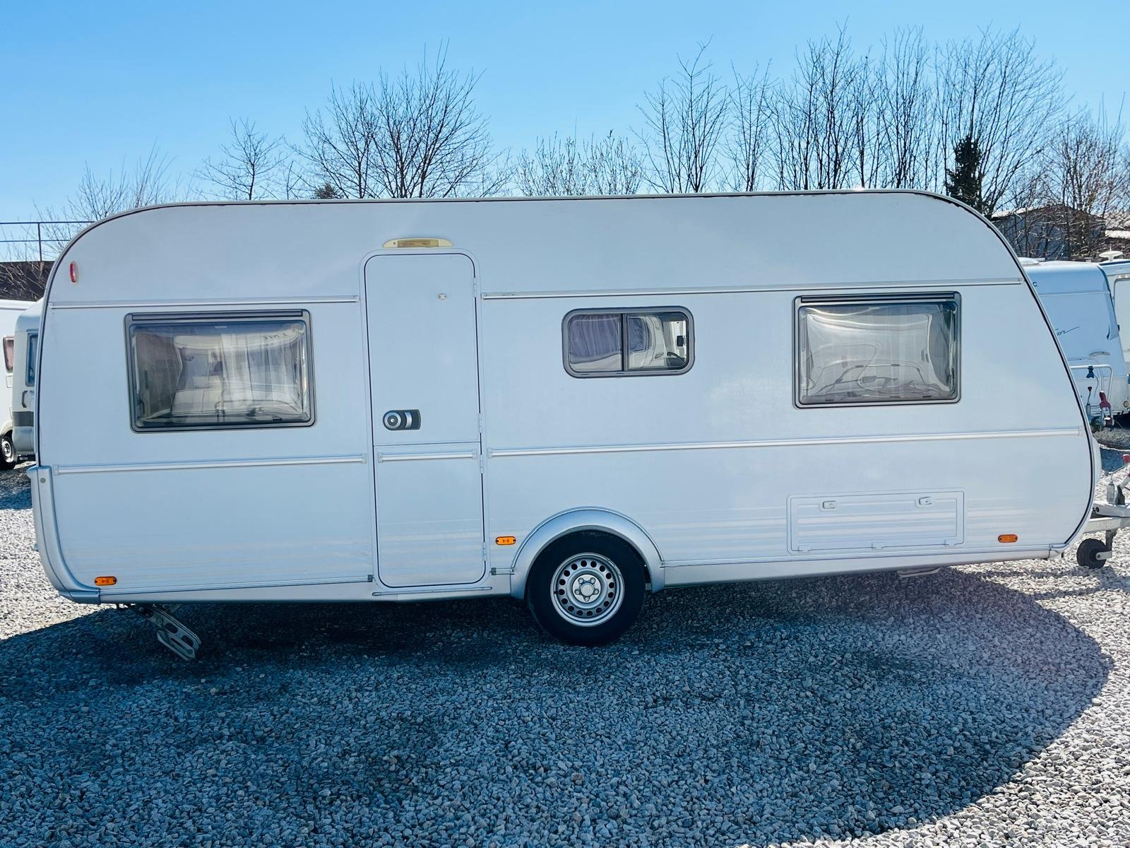 Bílý karavan bez viditelné značky, stojící na kamenitém povrchu. Ideální pro dovolené a kempování.