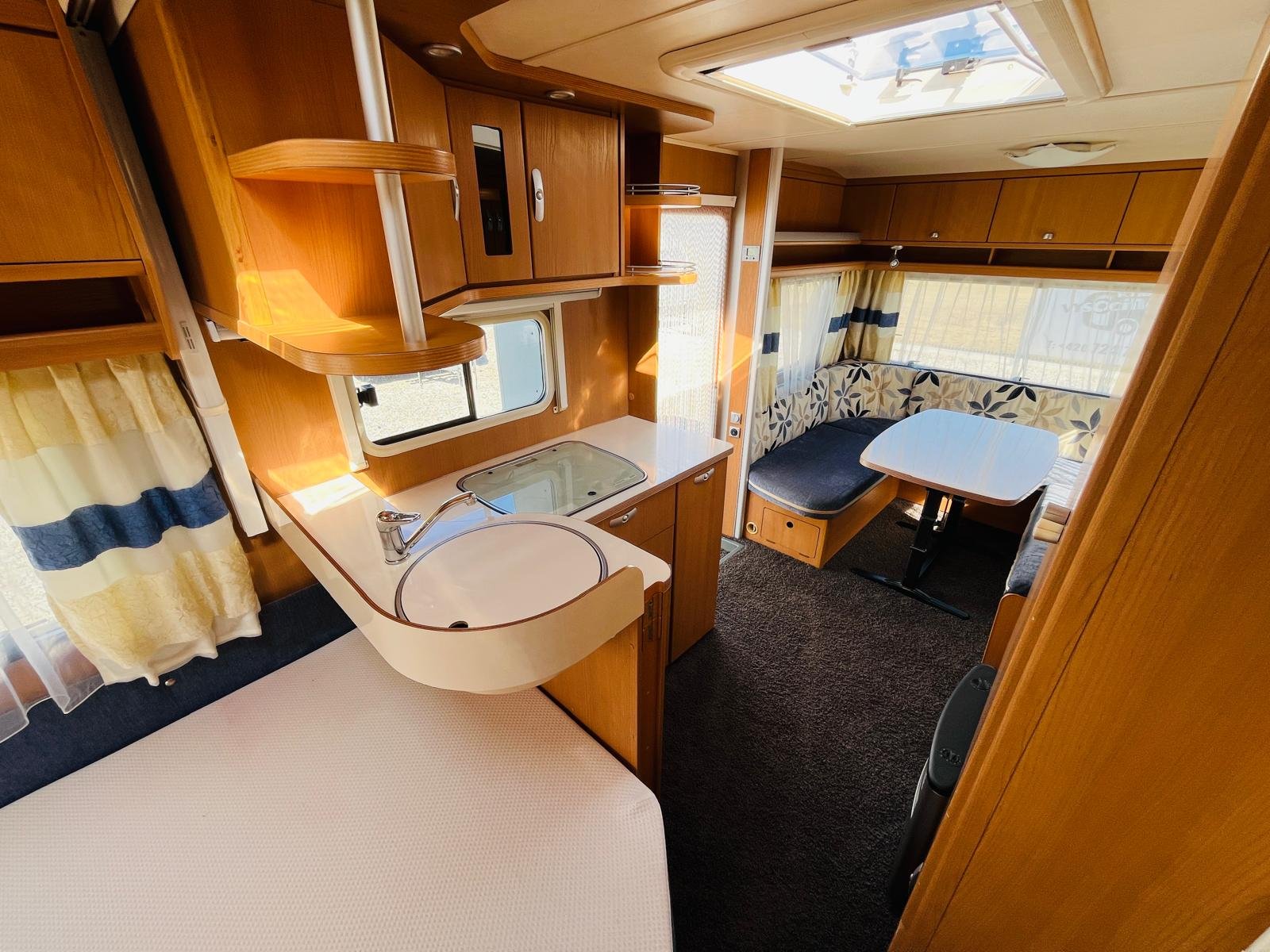 Interiér karavanu, stylové dřevo, kuchyňka a pohodlné posezení. Ideální pro pohodové cestování.