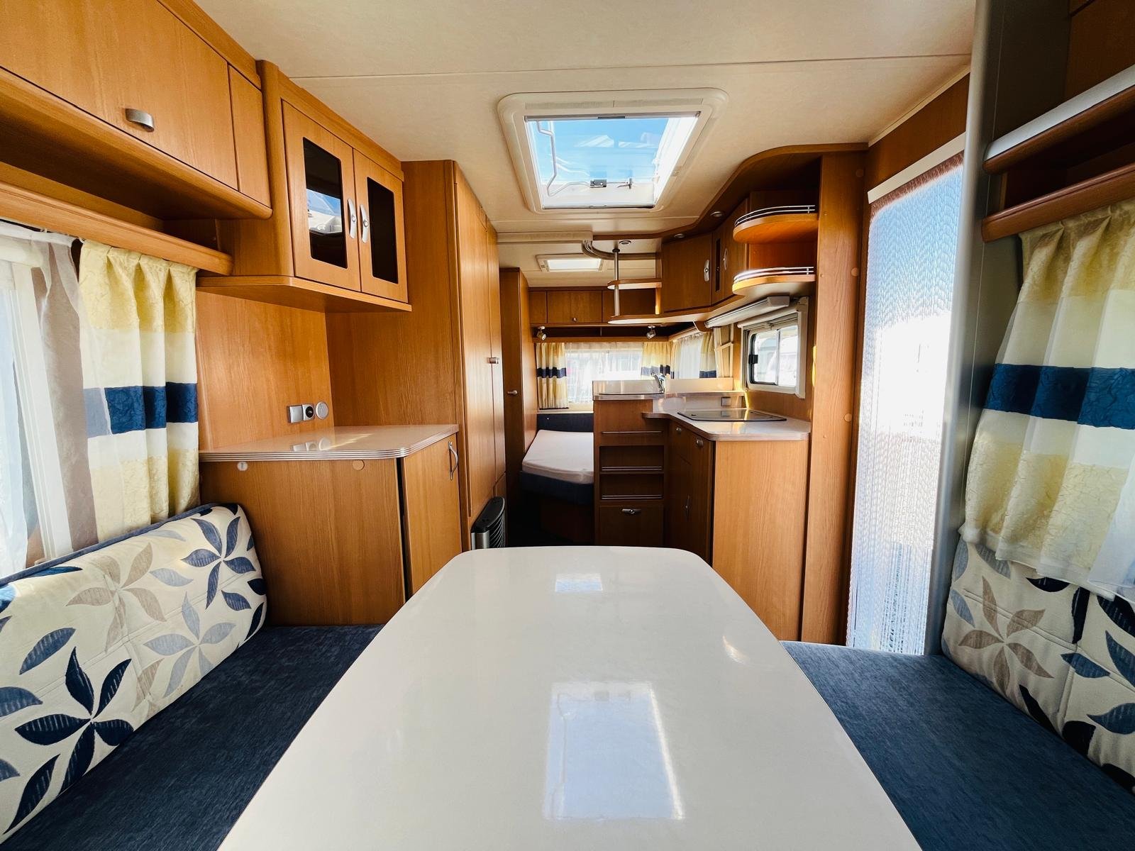 Obývací prostor karavanu s dřevěným interiérem, kuchyní a jídelním stolem, ideální pro pohodlné cestování.