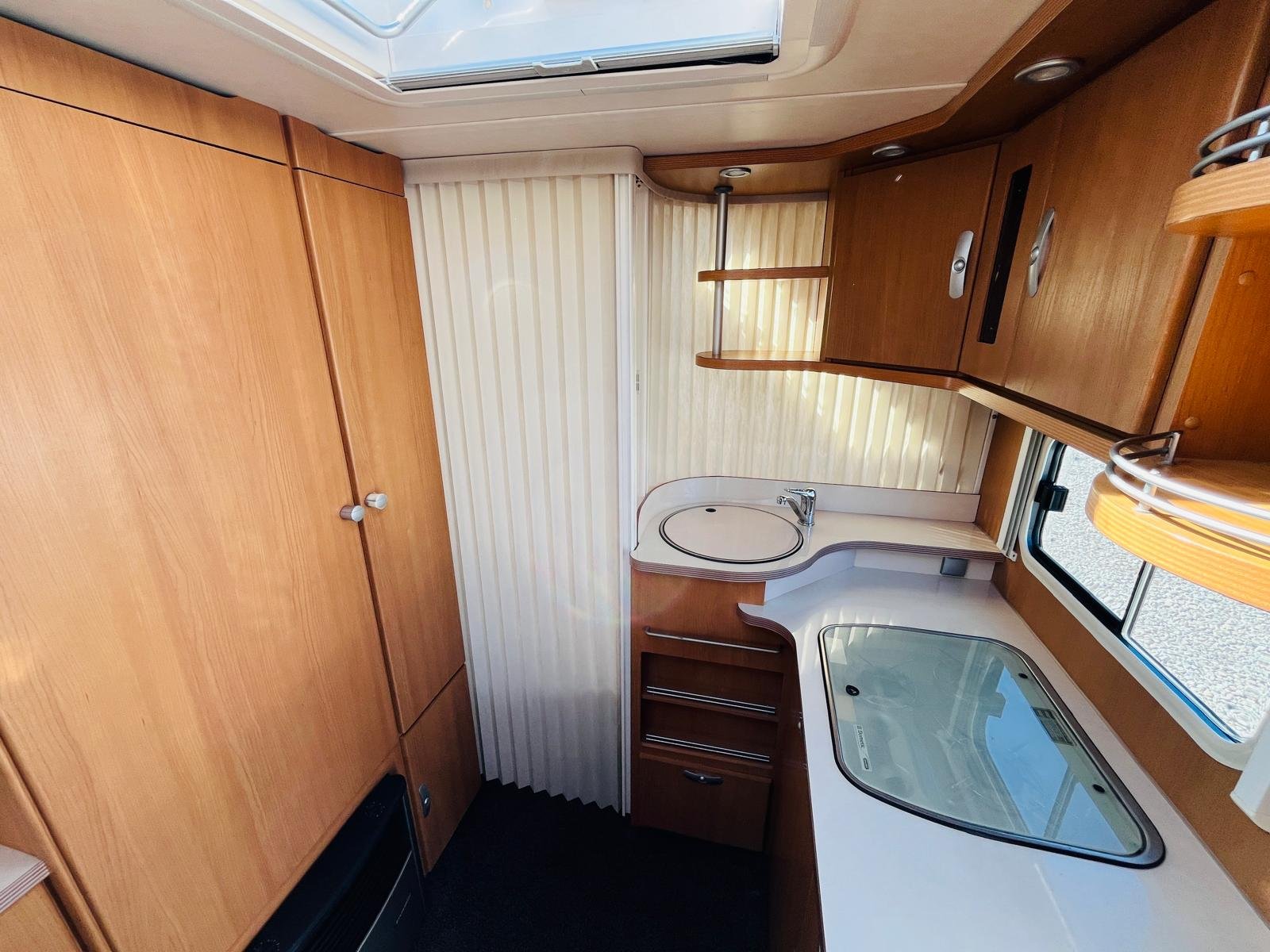 Interiér obytného auta s dřevěnými skříněmi a kuchyňským koutem. Příjemný a prostorný.