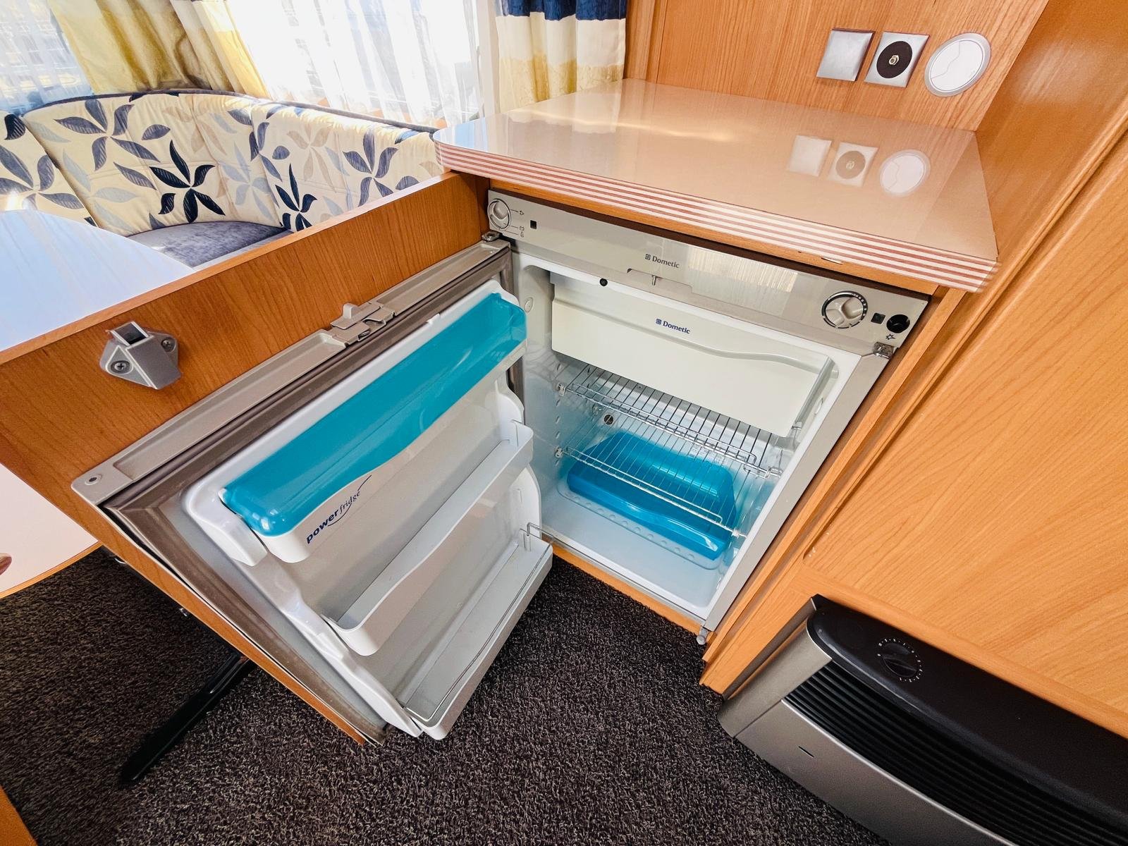 Obrázek interiéru obytného vozu s lednicí značky Dometic a pohodlným sezením. Ideální pro cestování.