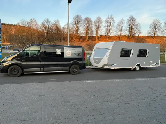 Obytné auto a karavan stojí na parkovišti, připravené na dobrodružství v přírodě. Modely nejsou viditelné.