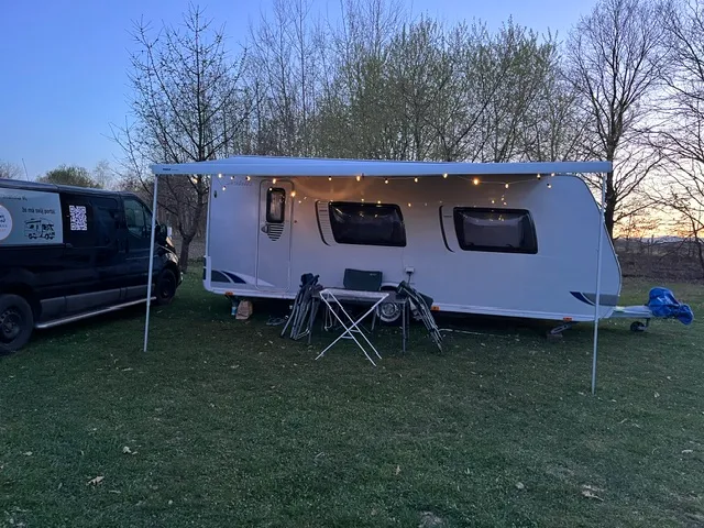 Na obrázku je karavan s venkovním posezením a osvětlením, ideální pro kempování.
