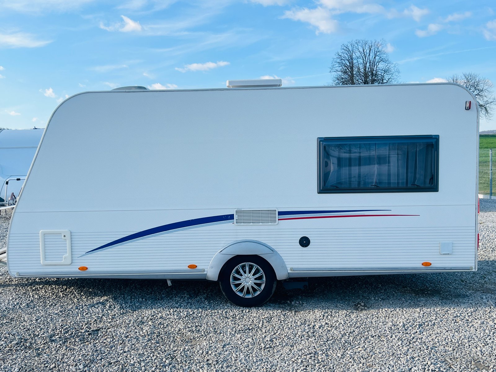 Bílý karavan s modrým dekorem, ideální pro cestování a kempování. Perfektní volba pro dobrodružství!