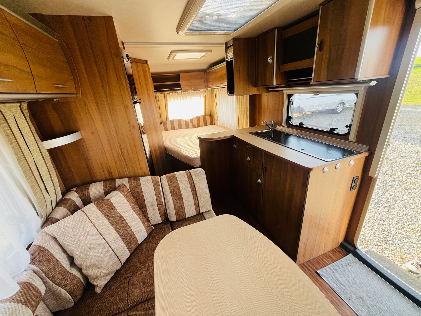 Obrázek interiéru karavanu s dřevěným nábytkem a pohodlným sezením. Čistý a prostorný design pro dovolenou.