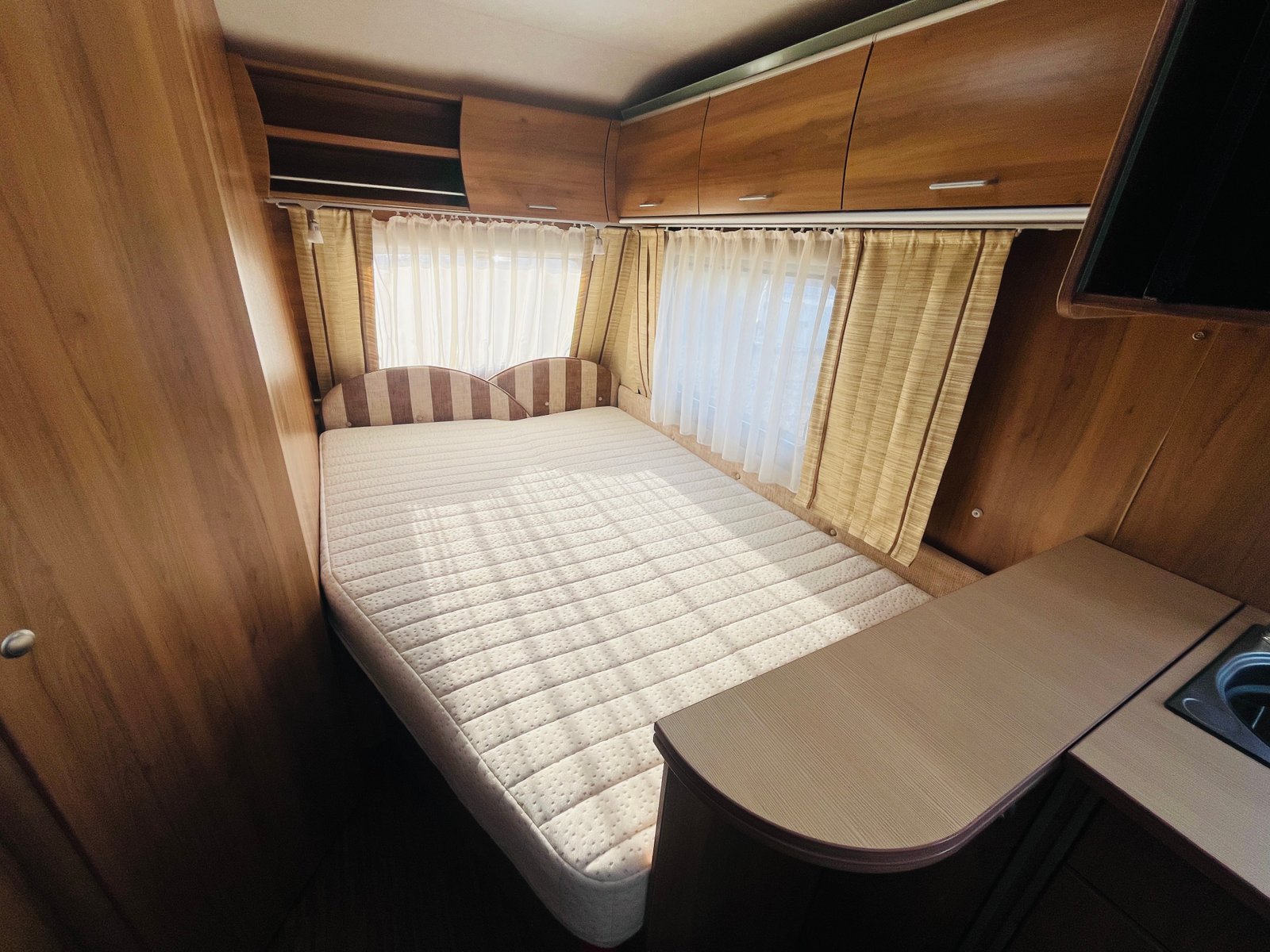 Interiér karavanu s pohodlnou manželskou postelí a dřevěnými prvky pro útulnou atmosféru.