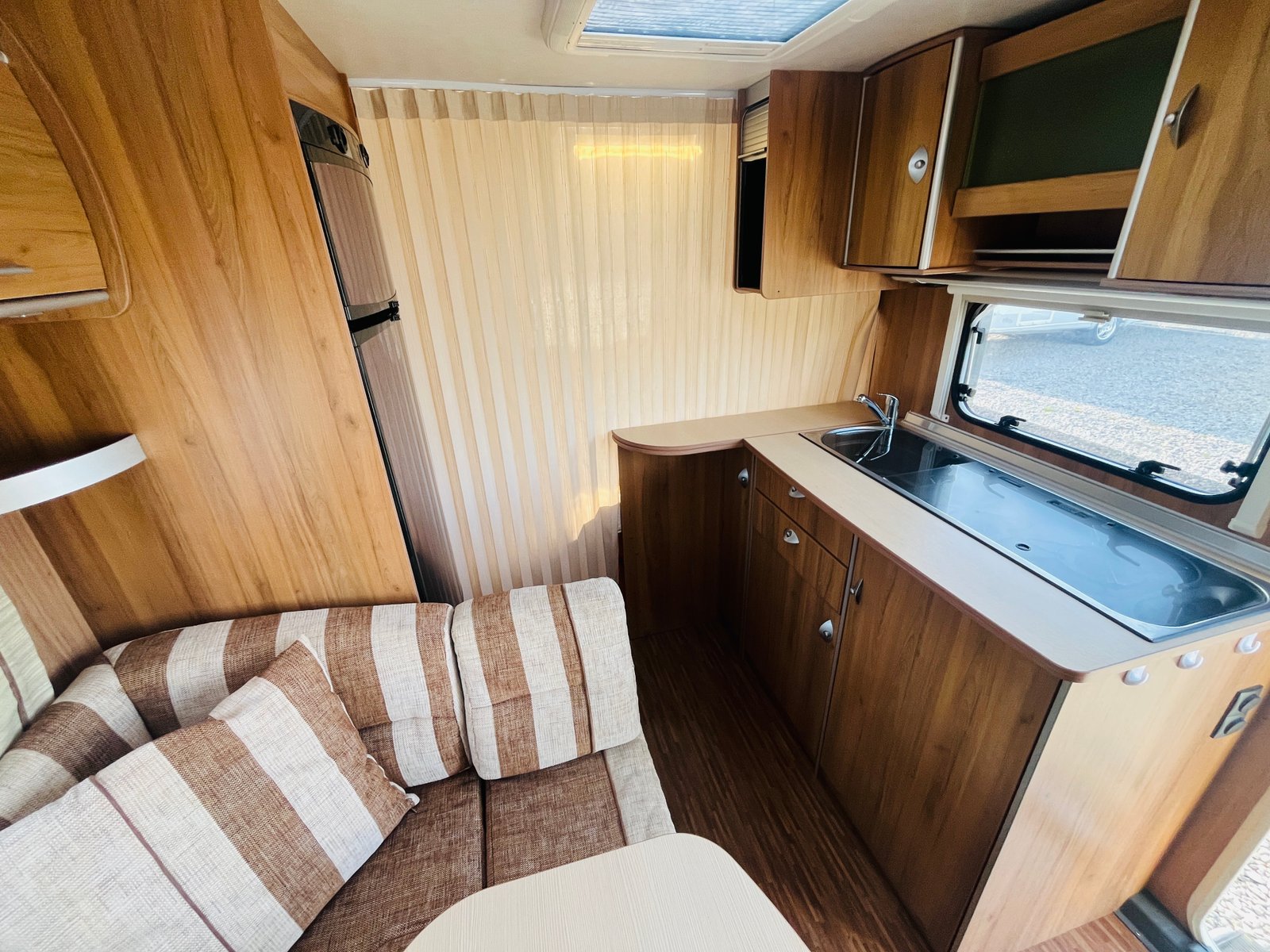 Interiér karavanu s dřevěnými prvky a stylovou sedačkou. Prostor včetně kuchyňského koutku.