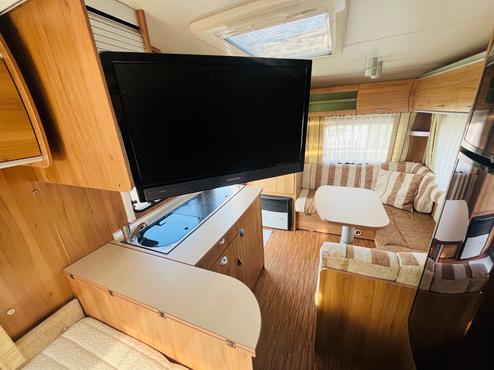 Interiér karavanu s pohodlným posezením, televizí a kuchyňským koutem. Ideální pro rodinné cestování a odpočinek.